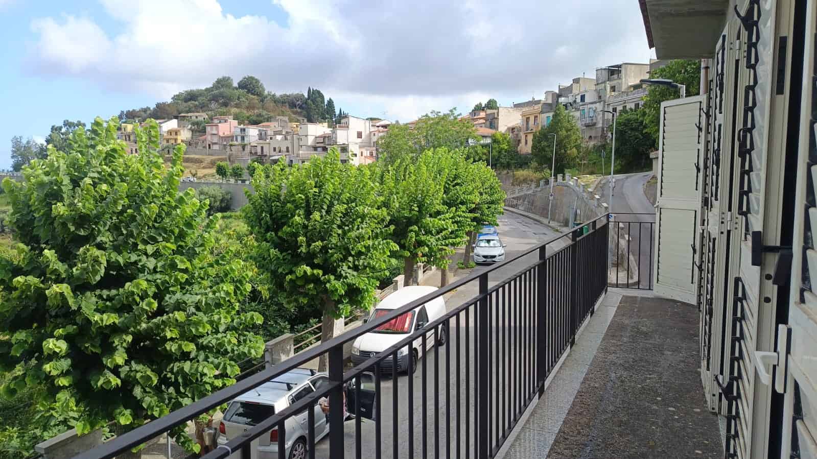 Veranda con vista su strada e case nel quartiere storico di NextCasa, con alberi verdeggianti e panorama urbano, ideale per relax e vita quotidiana.