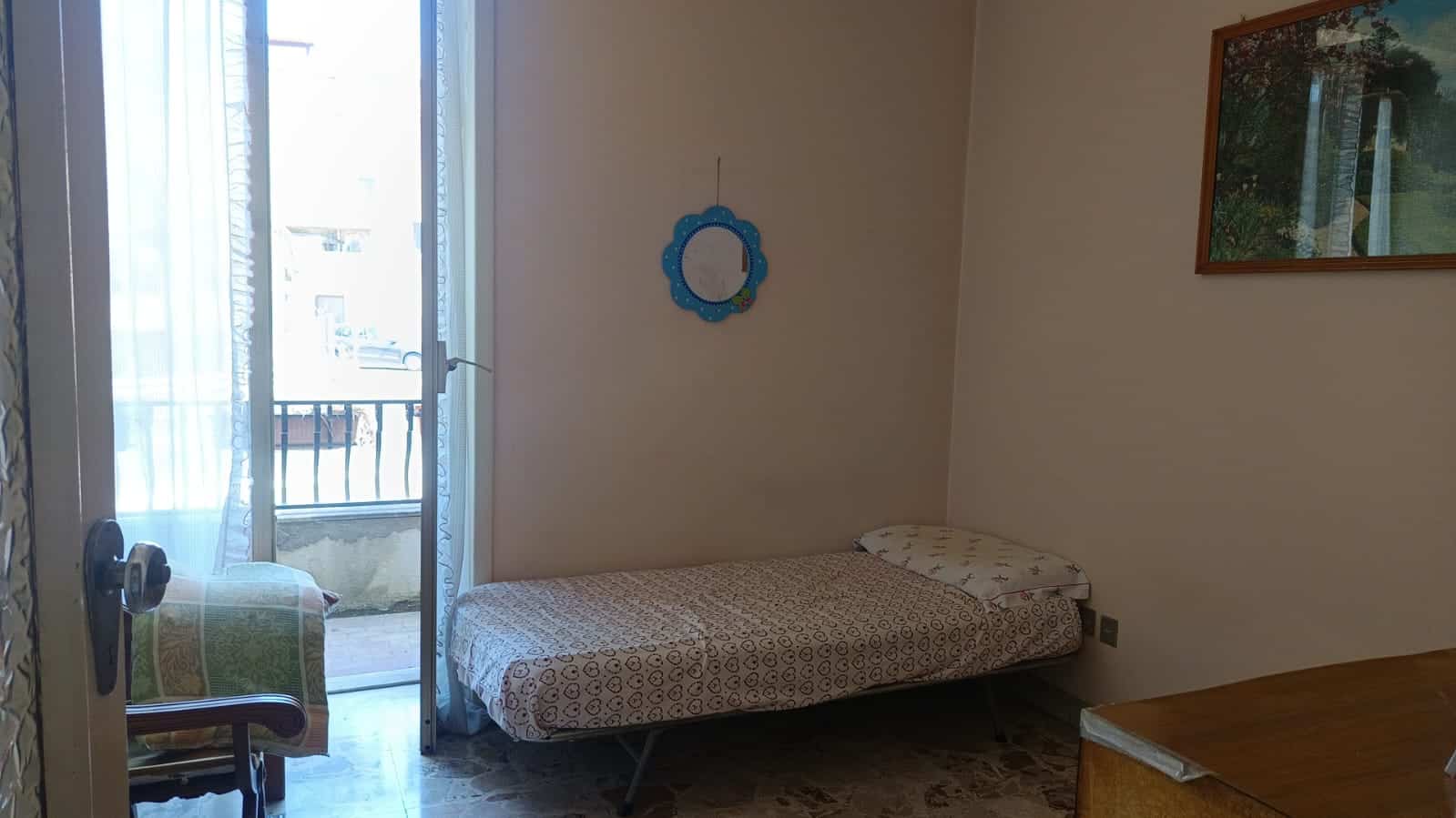 Letto singolo con balcone e vista, arredamento semplice e funzionale in appartamento NextCasa. Ideale soluzione abitativa in zone residenziali, mostra interni con luce naturale e spazio per relax.