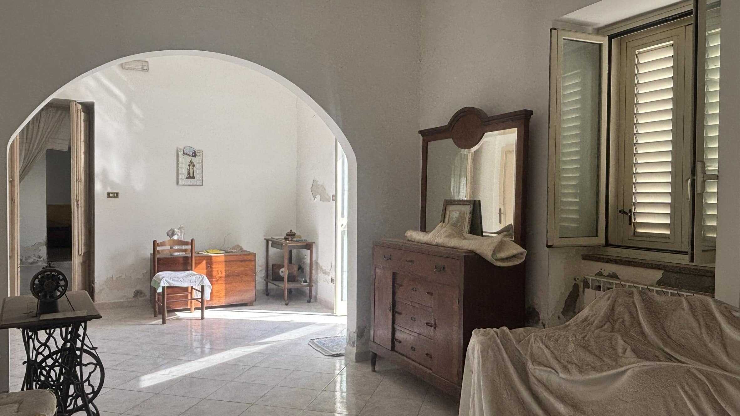 Antico interno di casa con mobili in legno, finestra con persiane e arredo vintage, atmosfera rustica e accogliente, immobile storico da ristrutturare.