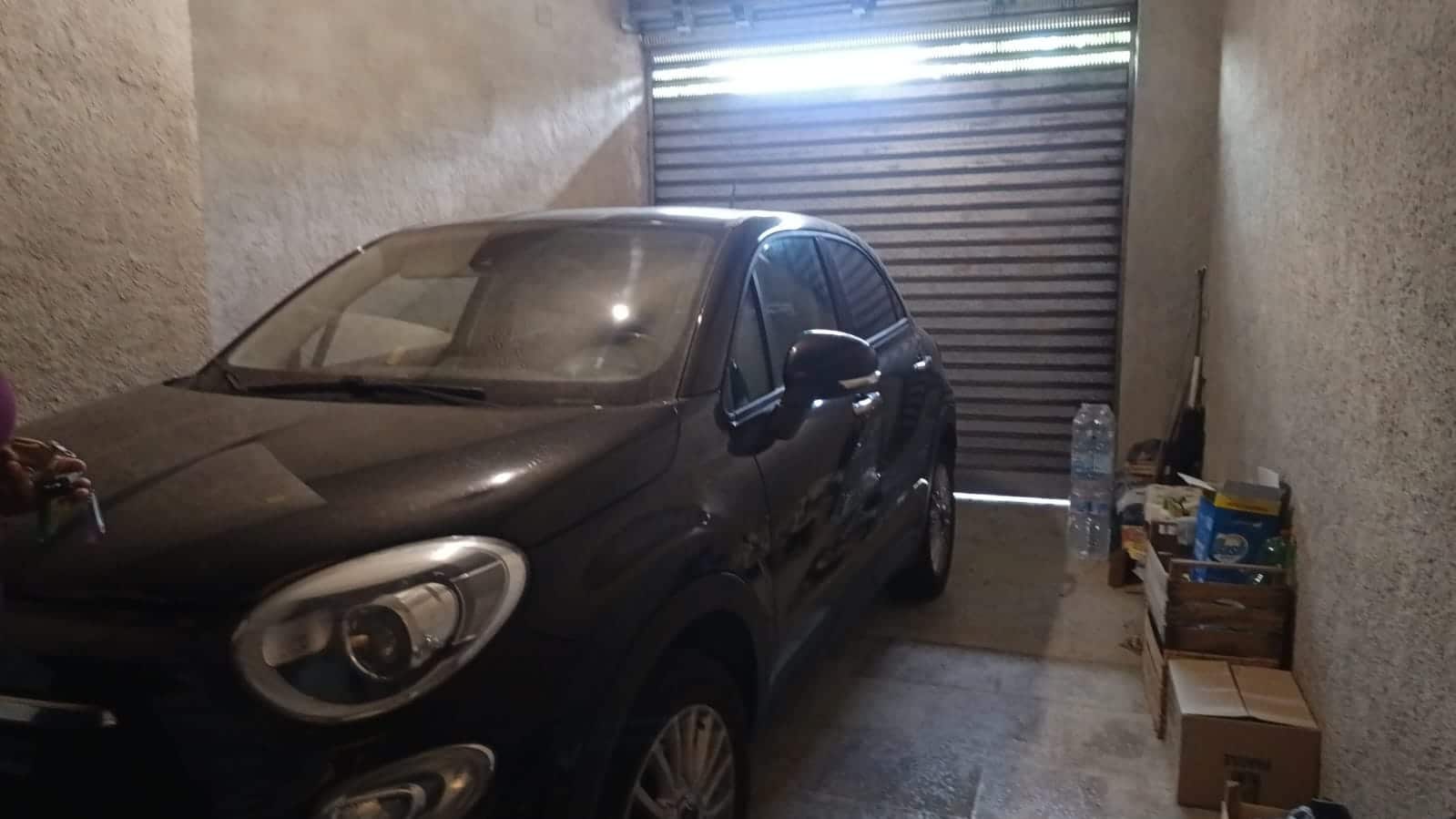 Box auto in garage, spazio di sosta per auto con pareti in muratura, serranda metallica e attrezzature di magazzino, ideale per la sicurezza e la protezione del veicolo.