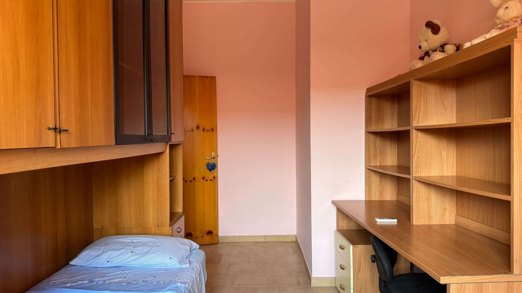 Sveglia in cameretta con mobili in legno, scrivania e scaffali spaziosi, arredo funzionale e accogliente, ambiente luminoso e ordinato, ideali per studenti e giovani adulti, arredamento pratico e moderno.