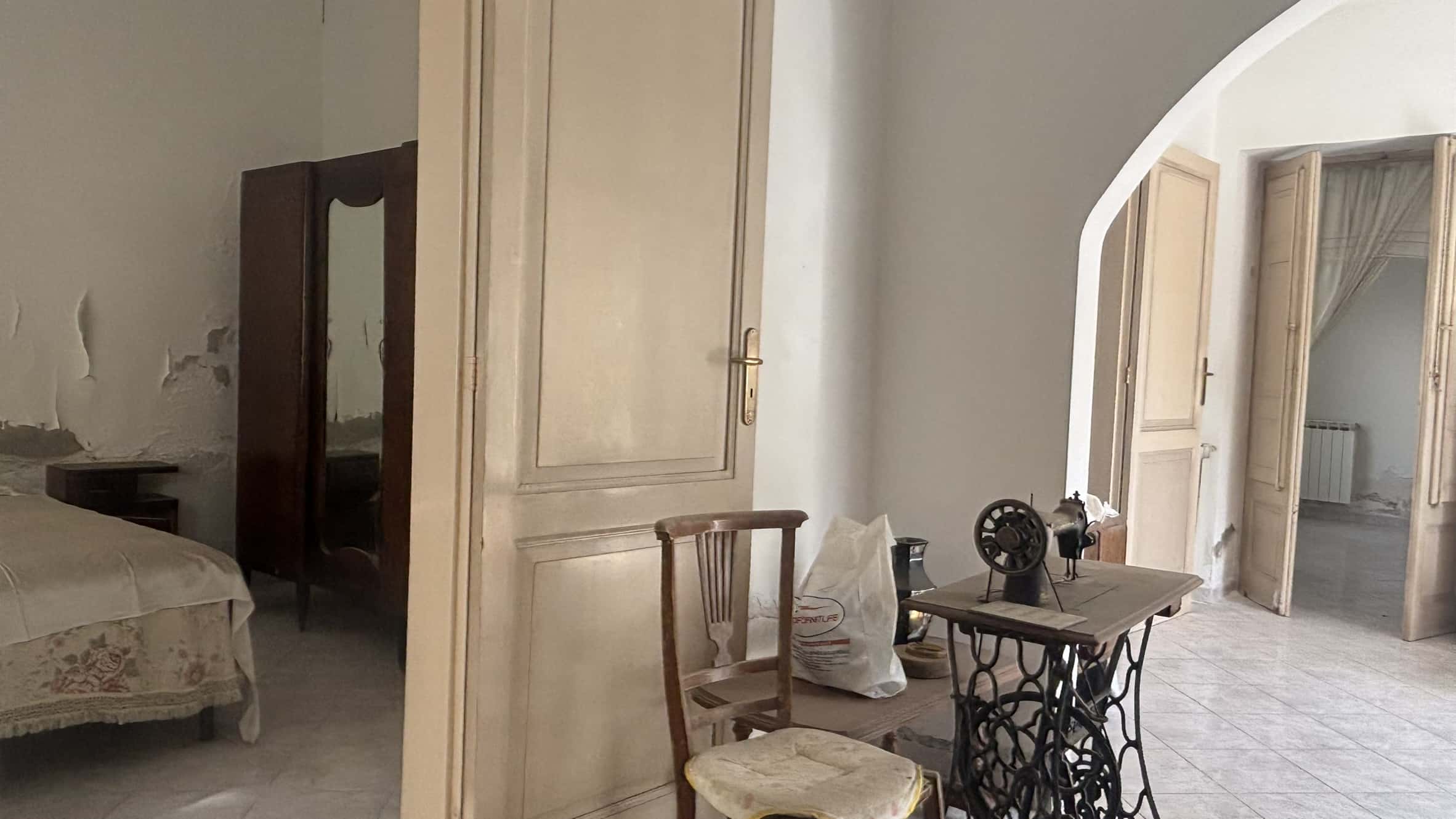 Vecchio arredamento per la casa in stile rustico con porta in legno e mobili vintage, ambiente abitativo in deterioramento, pareti con segni di usura e pavimento in piastrelle.