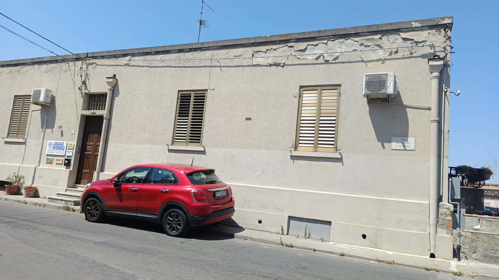 Auto in stile urbano parcheggiata davanti a edificio residenziale con finestre con persiane, aria condizionata e insegna linguistica, in centro città, immobile con segni di deterioramento, vista di strada.