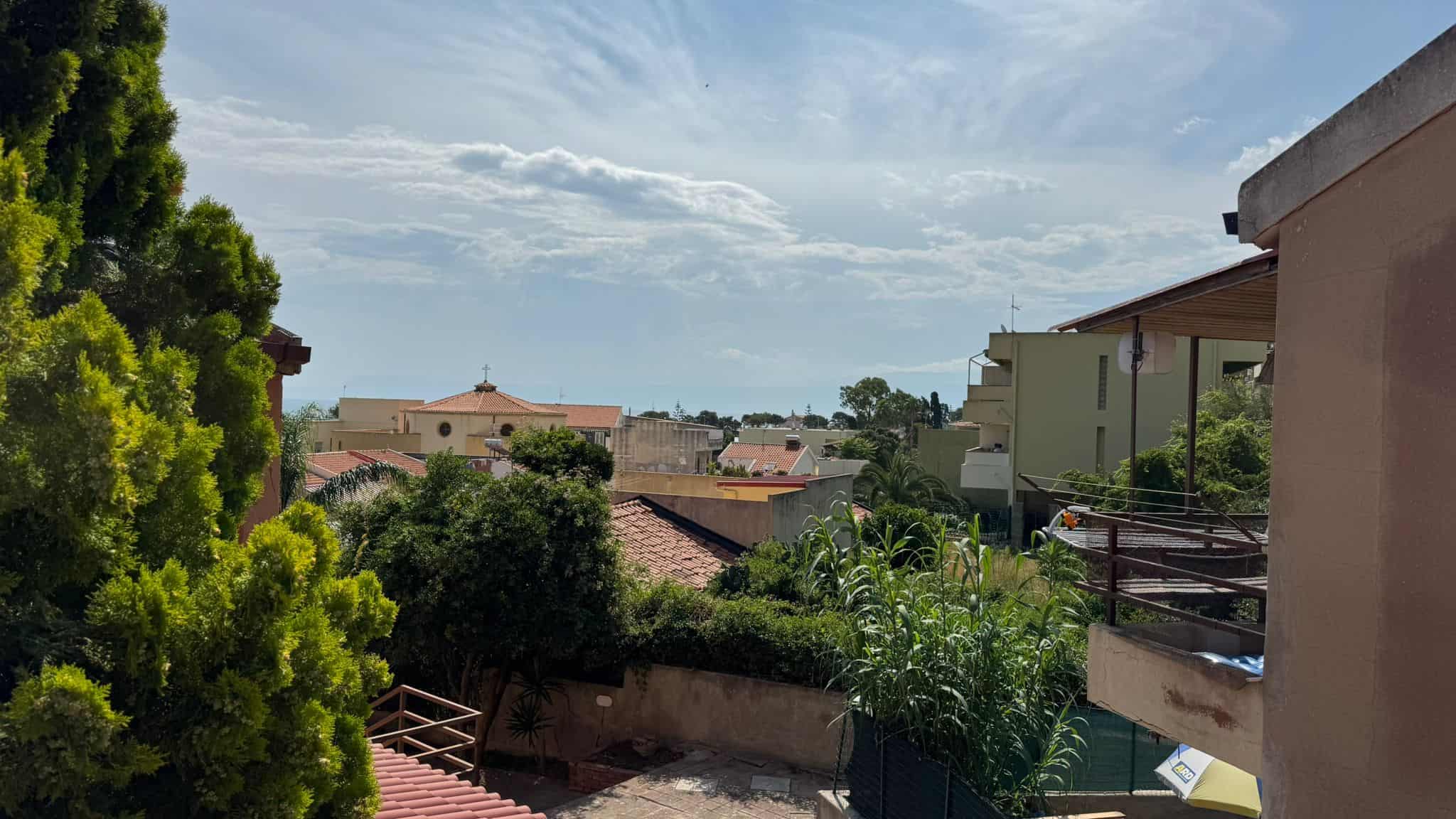 Vicinanze di case residenziali con vista panoramica sul quartiere, con alberi verdi, tetti in terracotta e cielo terso.