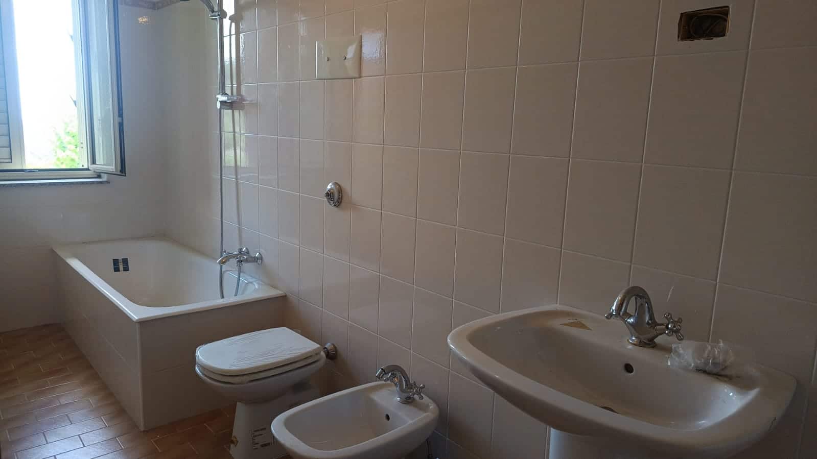 Bagno con vasca e bidet in appartamento privato NextCasa, stanze ideale per ristrutturare, pavimento in ceramica beige, finestra per luce naturale e aria fresca.