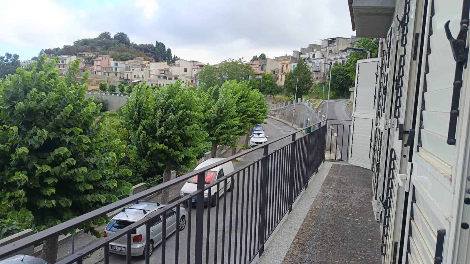 Balcone con vista su strada e case su collina in zona residenziale, con alberi e veicoli parcheggiati, atmosfera tranquilla e panoramica; immobile in vendita o affitto a NextCasa, agenzia immobiliare.