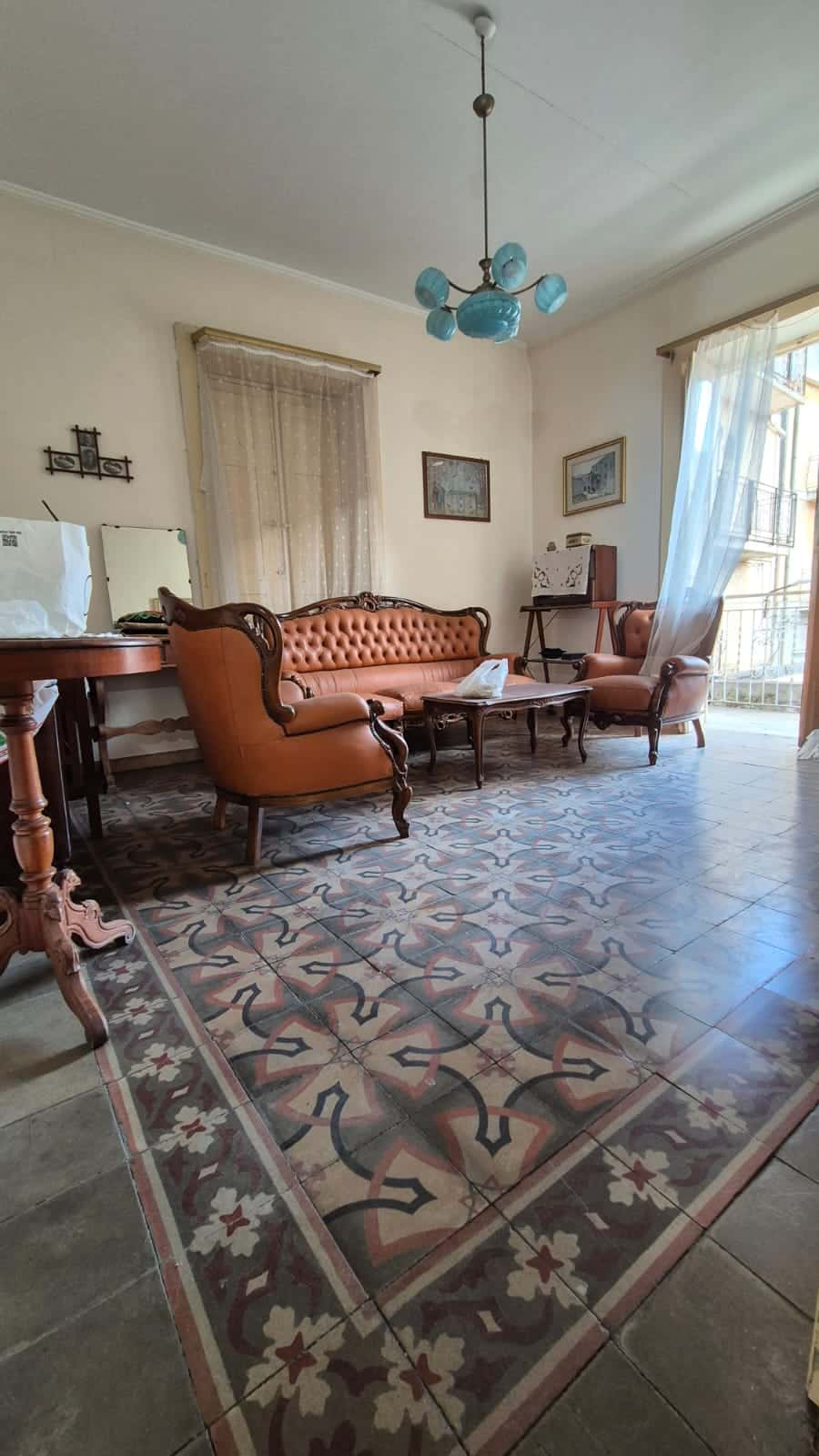 Antico salotto in stile classico con divani in pelle, mobili in legno e piastrelle decorate, ambiente luminoso con tende leggere, perfetto per soggiorni accoglienti e eleganti.