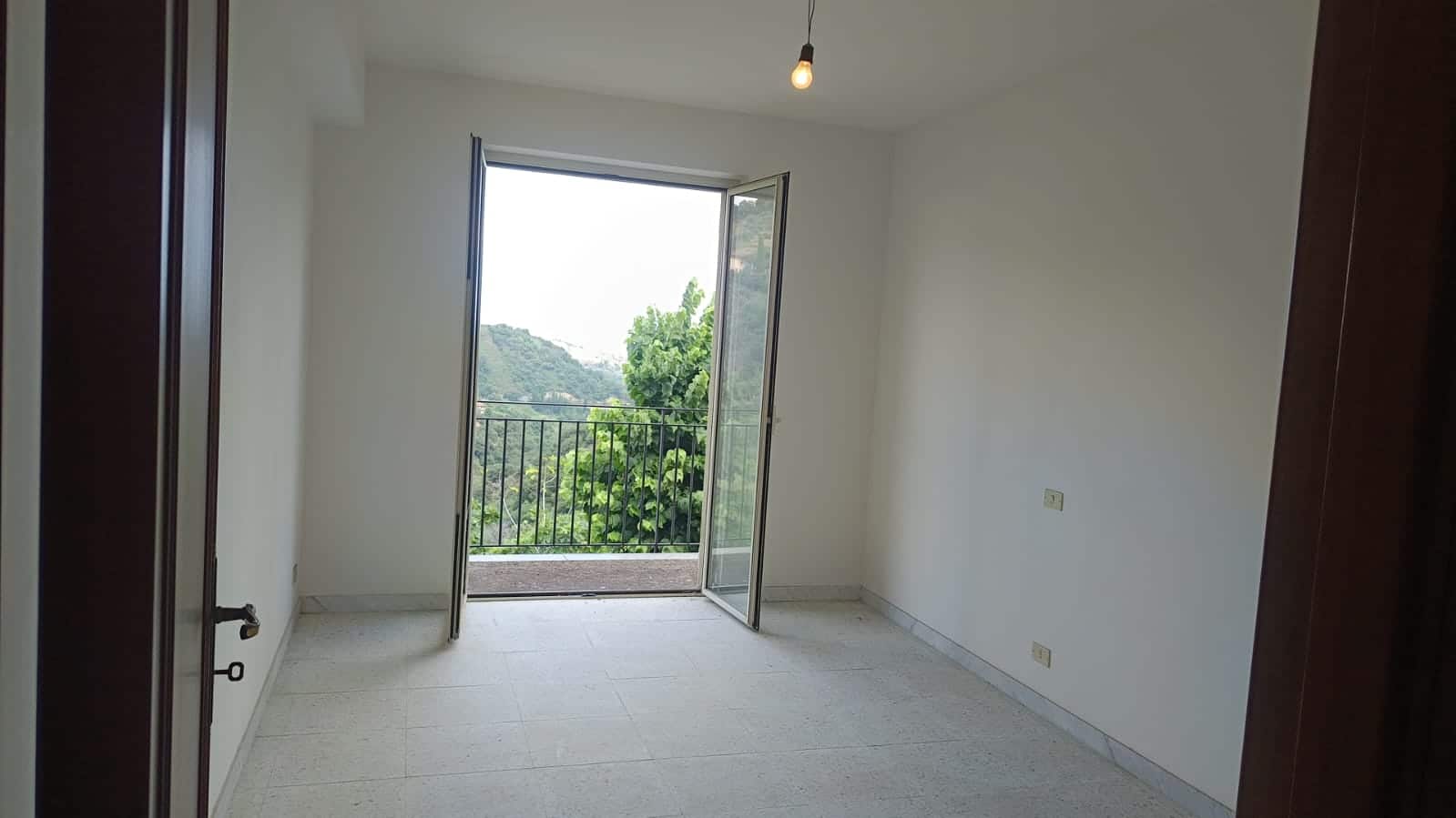 Balcone con vista verde e appartamento vuoto, spazio luminoso e arioso, ideale per residenza moderna, con porte in legno e pareti bianche.