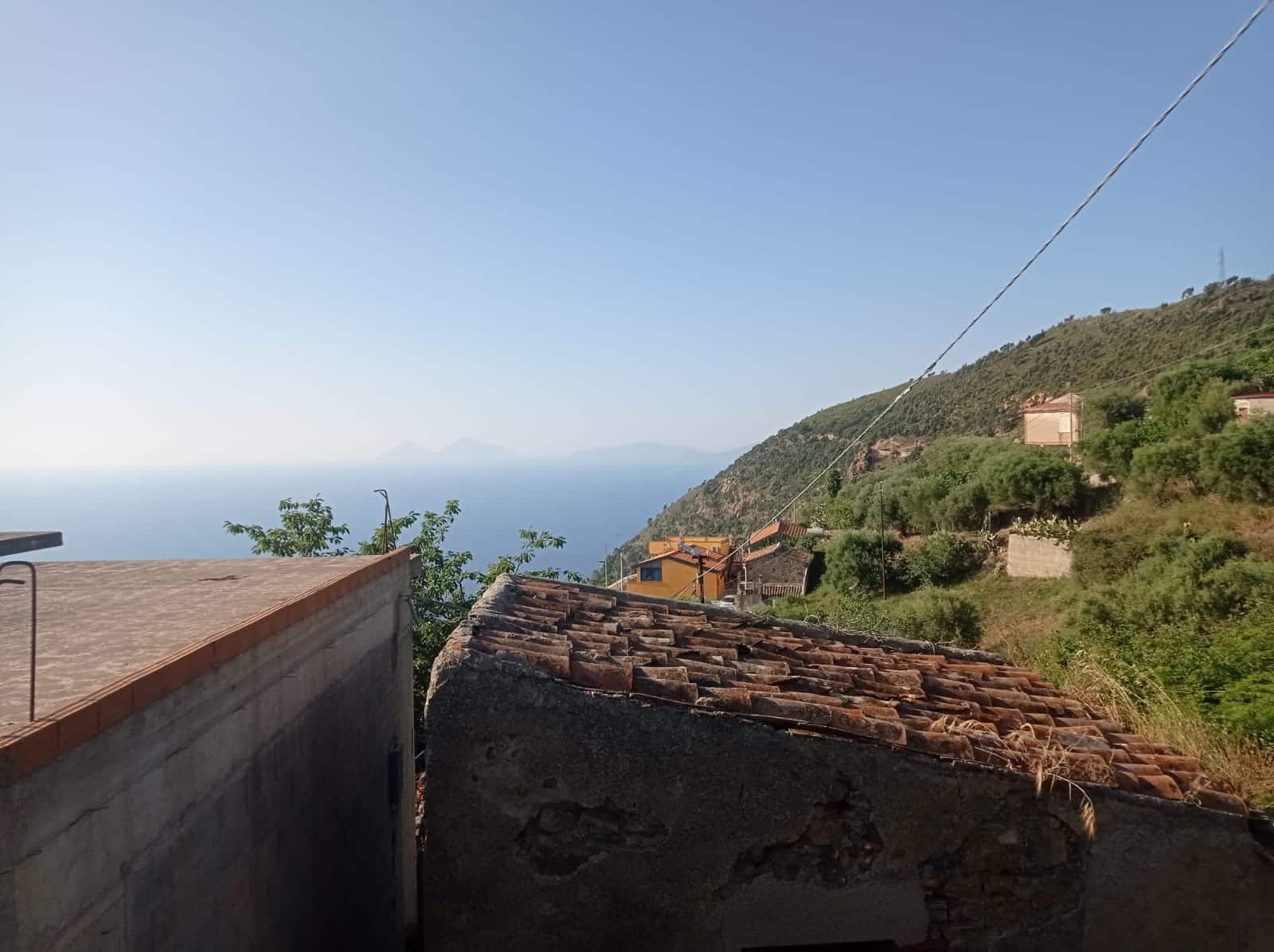 Vista panoramica sulla costa e sulla natura dalla terrazza di una casa in collina vicino al mare, caratterizzata da tetti in terracotta e paesaggi verdi, ideale per investimenti immobiliari a NextCasa.