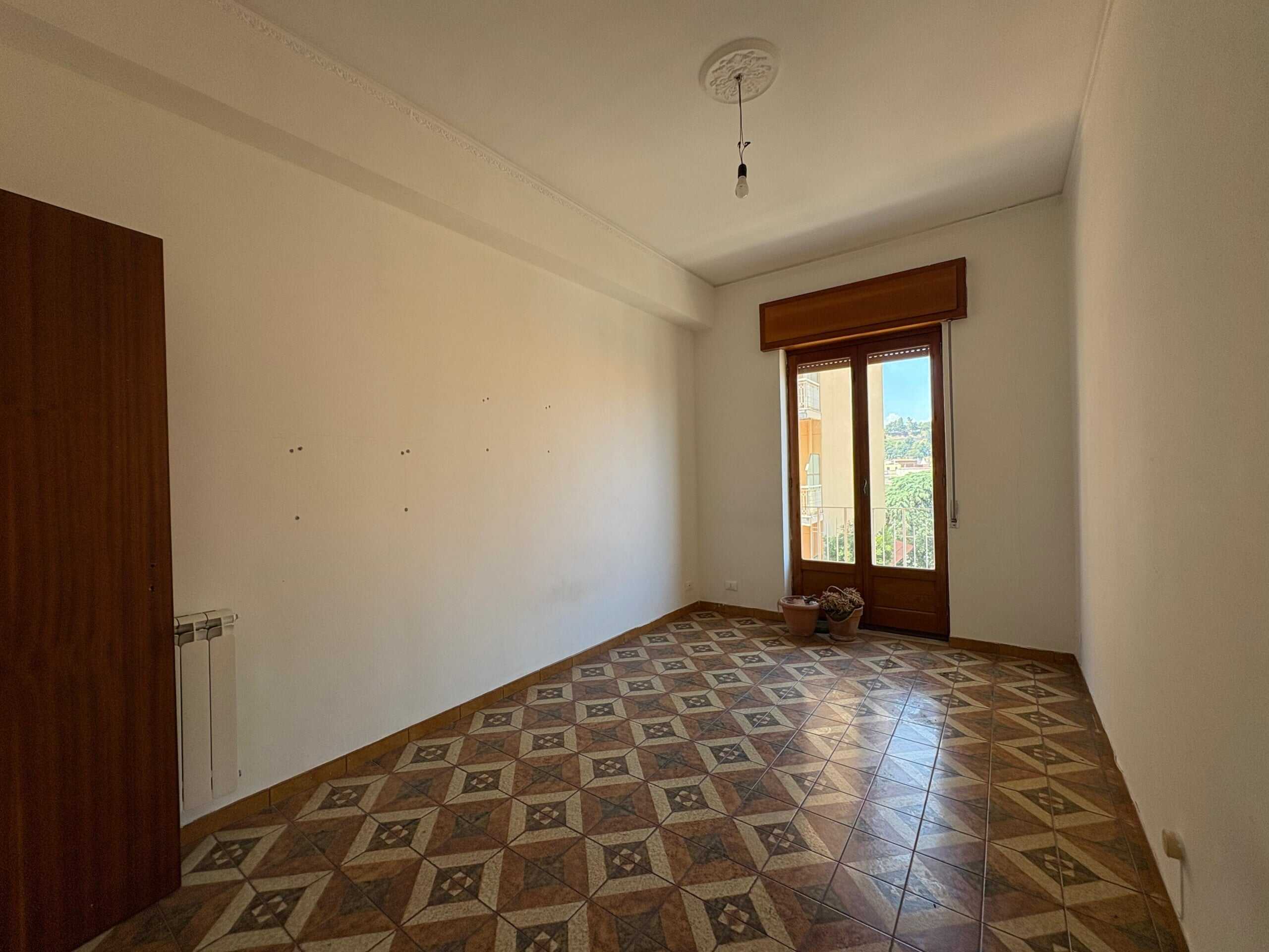 Abbastanza grande, luminoso e vuoto stanza da letto in appartamento in affitto con parquet in stile vintage e grande finestra che dà su un balcone e offre vista panoramica sulla città in zona residenziale.