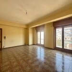 Ampio soggiorno luminoso con grandi finestre e balcone, pavimentazione in gres porcellanato e pareti neutre, perfetto per creare ambienti accoglienti e funzionali.
