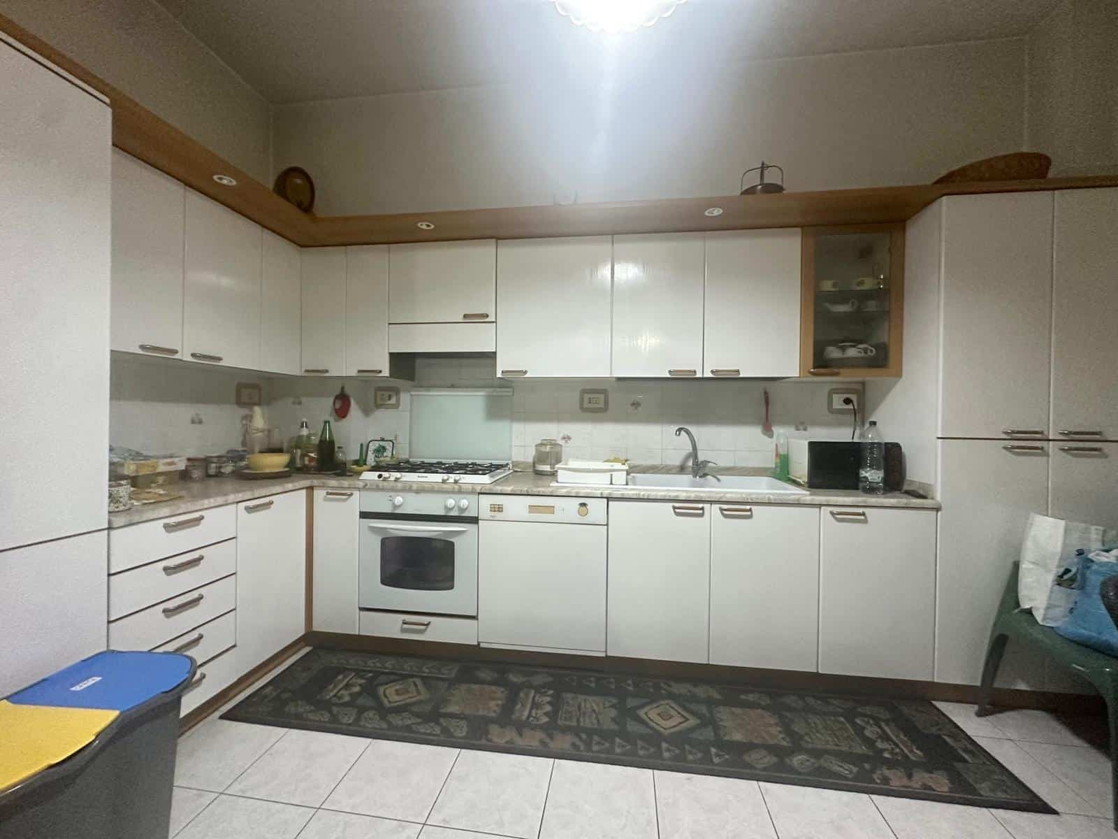 Immagine di una cucina abitabile con mobili bianchi, piano cottura, forno e lavello, decorata con dettagli in legno, utensili da cucina e elettrodomestici, ambiente luminoso e funzionale.