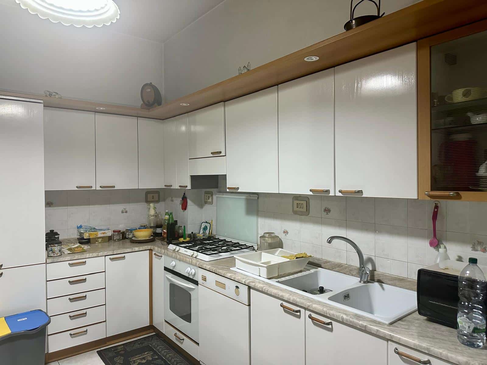 Cucina abitativa con ante bianche, piano in marmo chiaro, lavello doppio e elettrodomestici, in stile classico.
