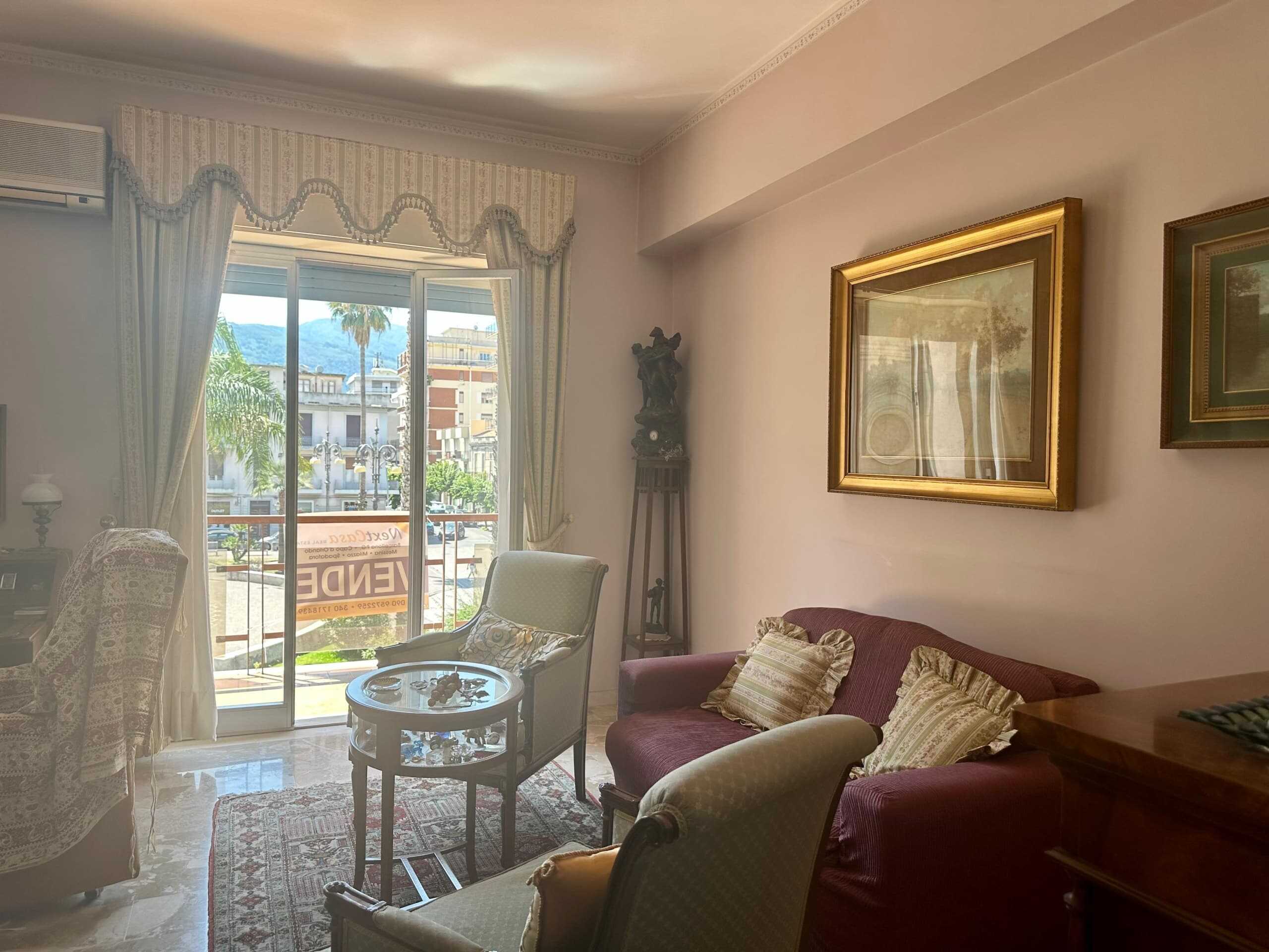 Vetrina di un soggiorno elegante e luminoso con grandi finestre, arredamento classico con poltrone, divano con cuscini, quadri dorati alle pareti, decorazioni d'epoca e view sulla città e montagne sullo sfondo.