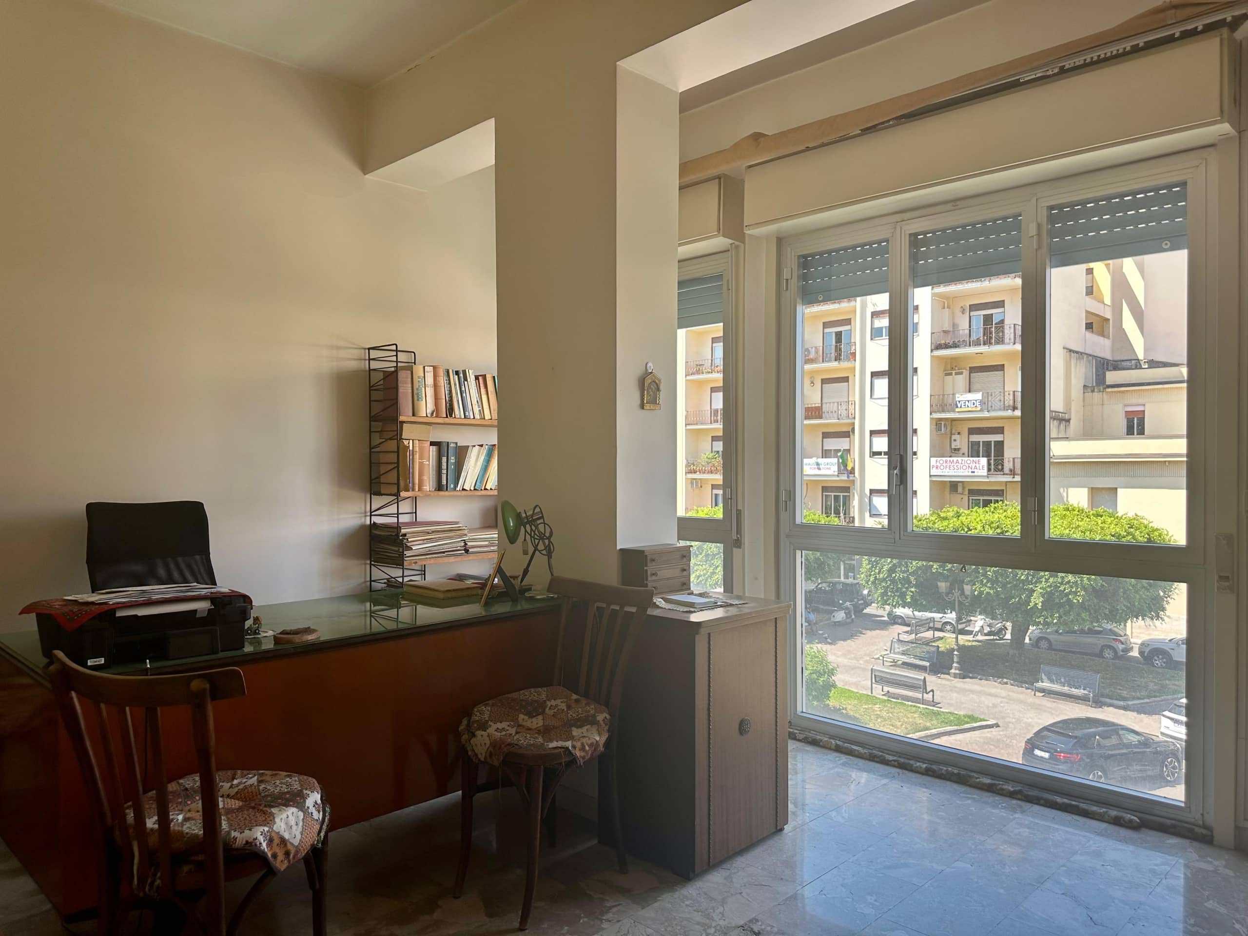 Elegante ufficio con grandi finestre che offrono luce naturale, arredi funzionali e scaffale con libri, ideale per spazi di lavoro professionali a Milano.