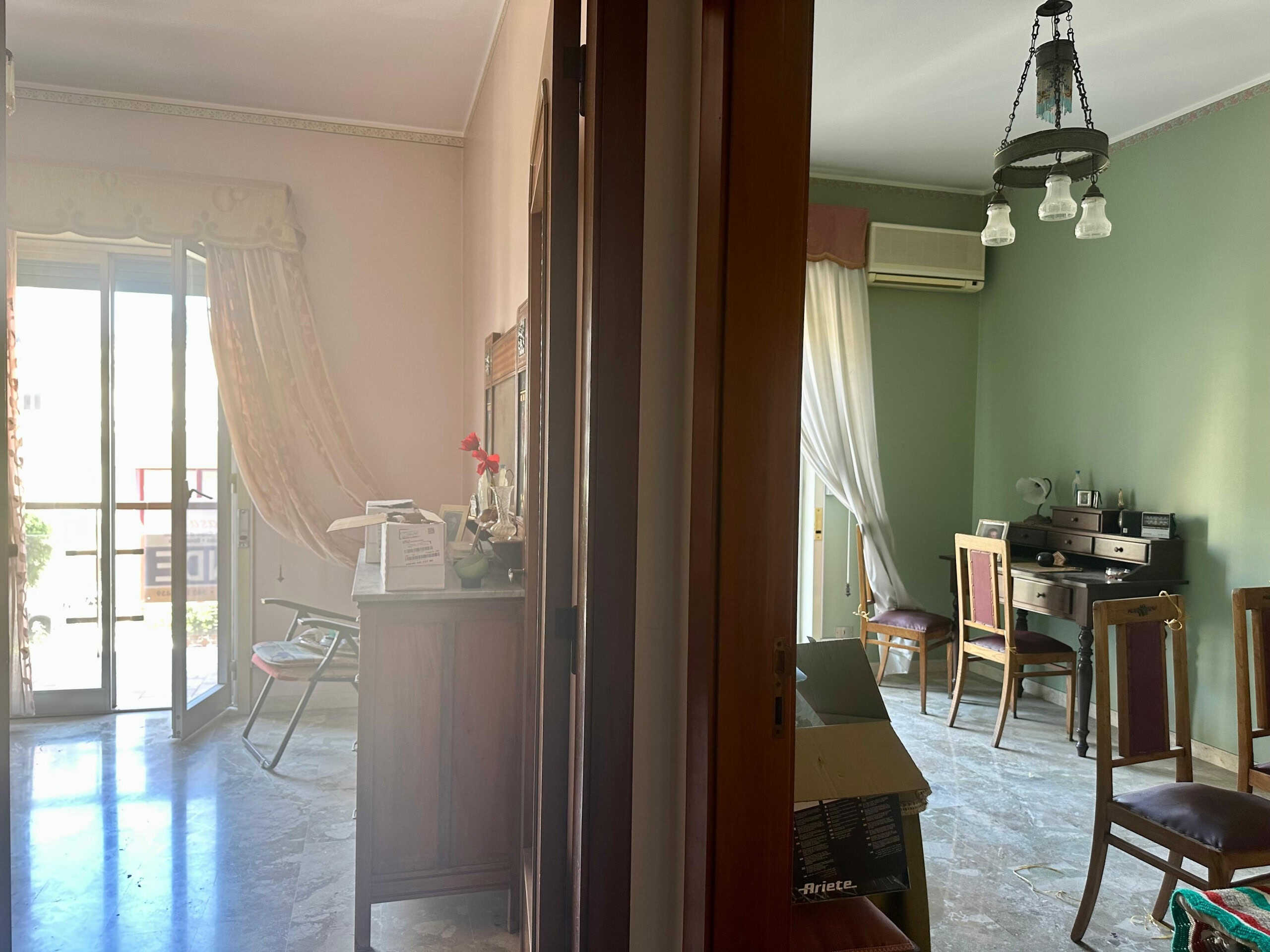 Riflesso di interni di casa con ingresso luminoso e sala da pranzo con pareti verdi e mobilio classico, illuminato da lampadario antico e naturale luce che entra dalle finestre con tende eleganti.