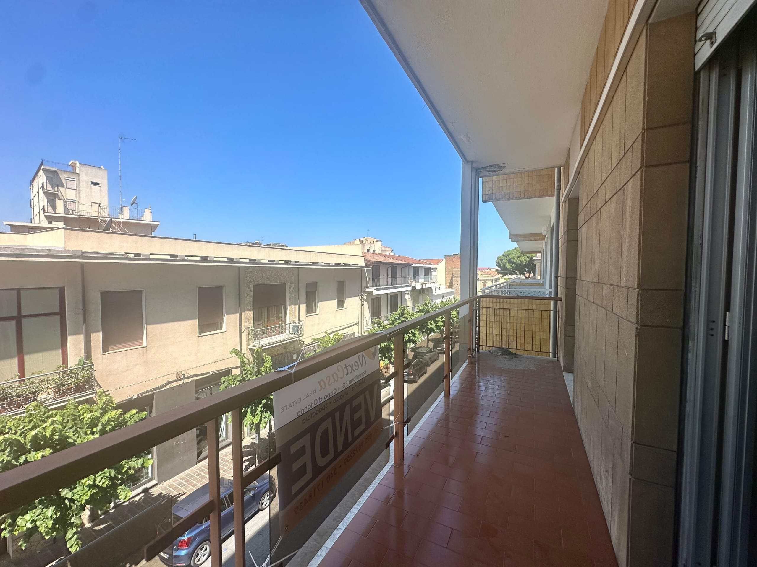 Balcone di un appartamento con vista sulle case vicine, pavimento in piastrelle rosse, in zona residenziale con cielo sereno e edificio moderno in primo piano.