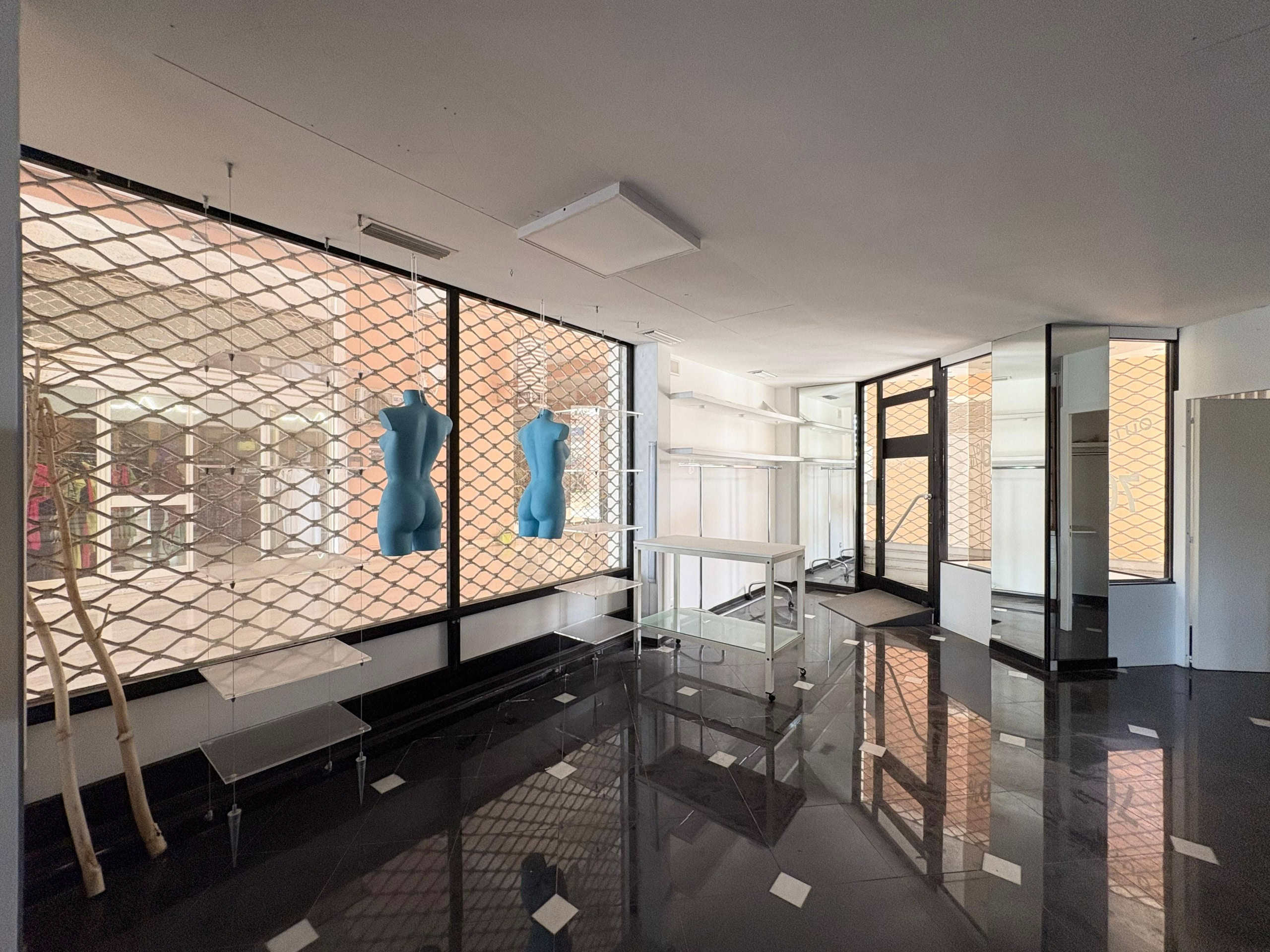 IMG-20250710-WA0005 Vetrina commerciale con ampie finestre e decorazioni di manichini blu, spazio moderno ideale per esposizioni di moda o negozi di abbigliamento, con pavimento lucido e struttura minimalista.
