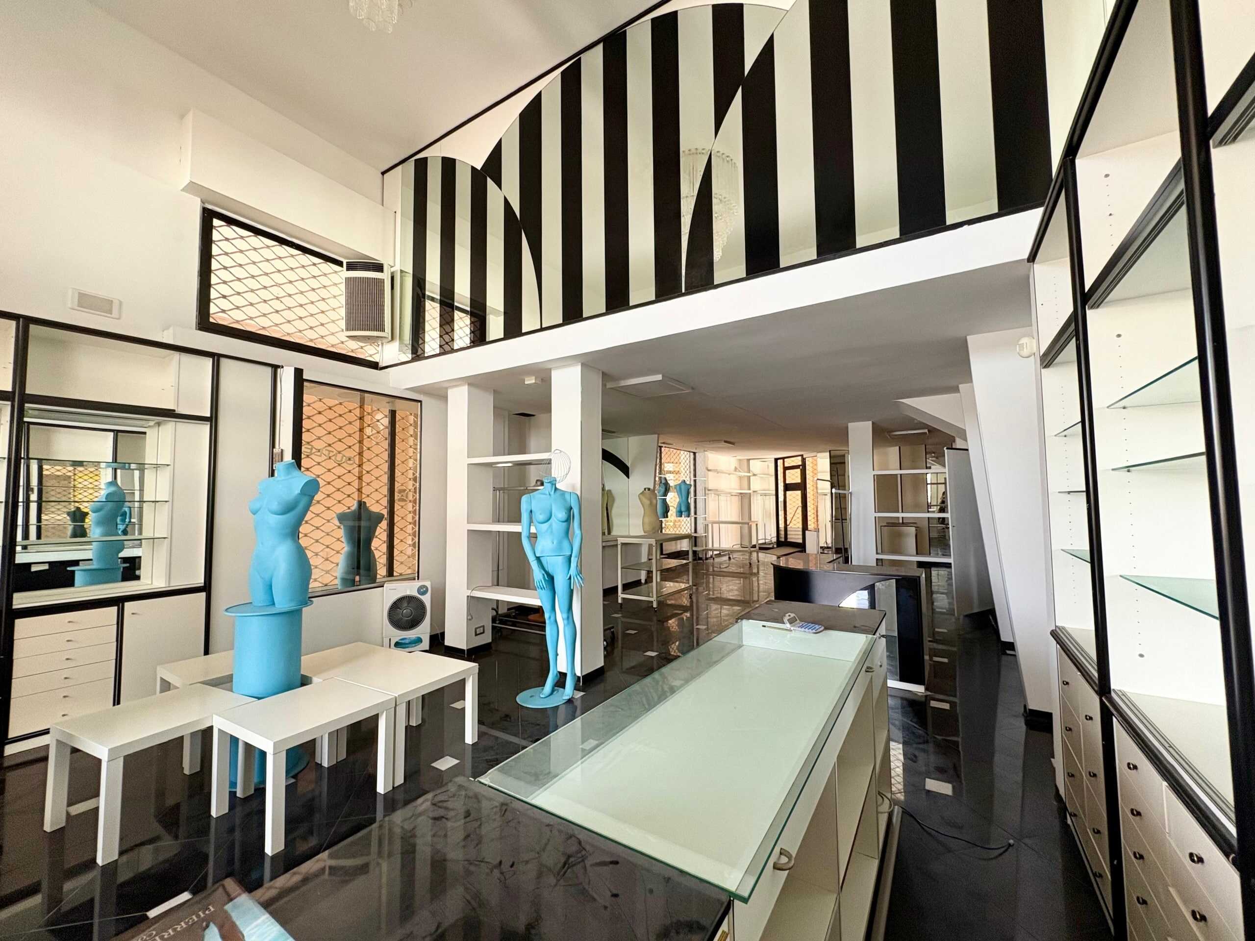 Manichini color azzurro e esposizione di arredamento negozio moda, con scaffali e specchi, ambiente luminoso e moderno, all’interno di un negozio di abbigliamento o accessori di moda.