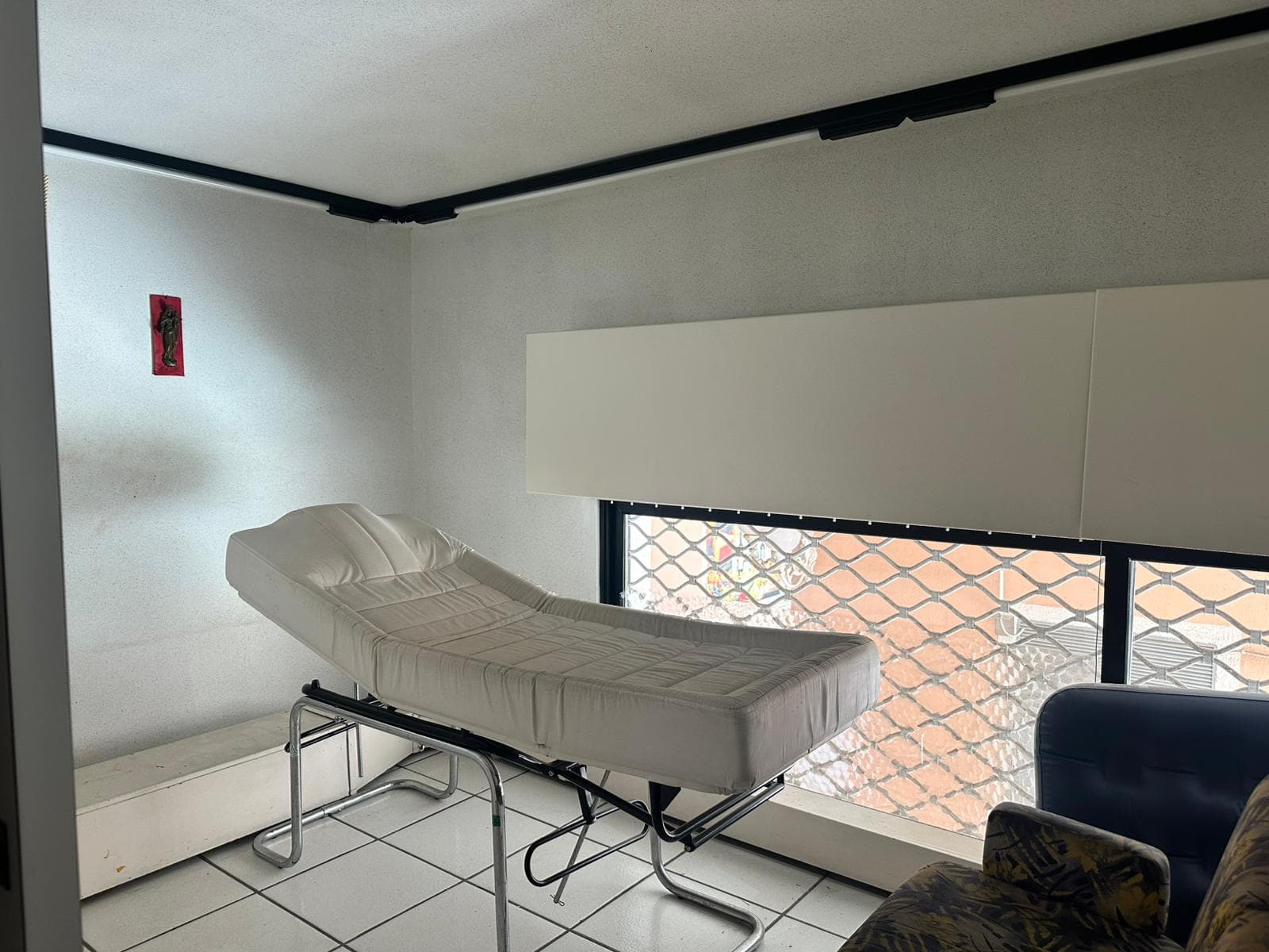 Letto medico esaminativo in uno studio medico con finestra protetta, arredo professionale, ambiente clinico ben illuminato e attrezzature di assistenza sanitaria per diagnosi e cure.