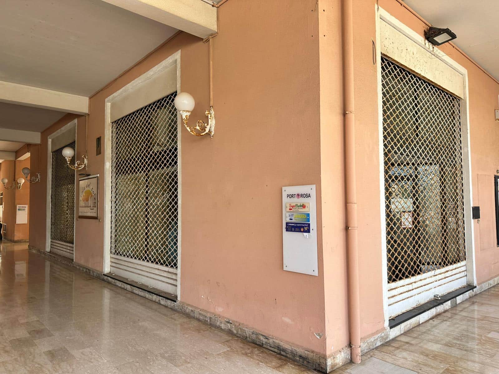 Portone commerciale con grate di sicurezza in un edificio residenziale vicino al porto, con illuminazione a parete e decorazioni classiche, ideale per ambienti di ospitalità e attività commerciali.