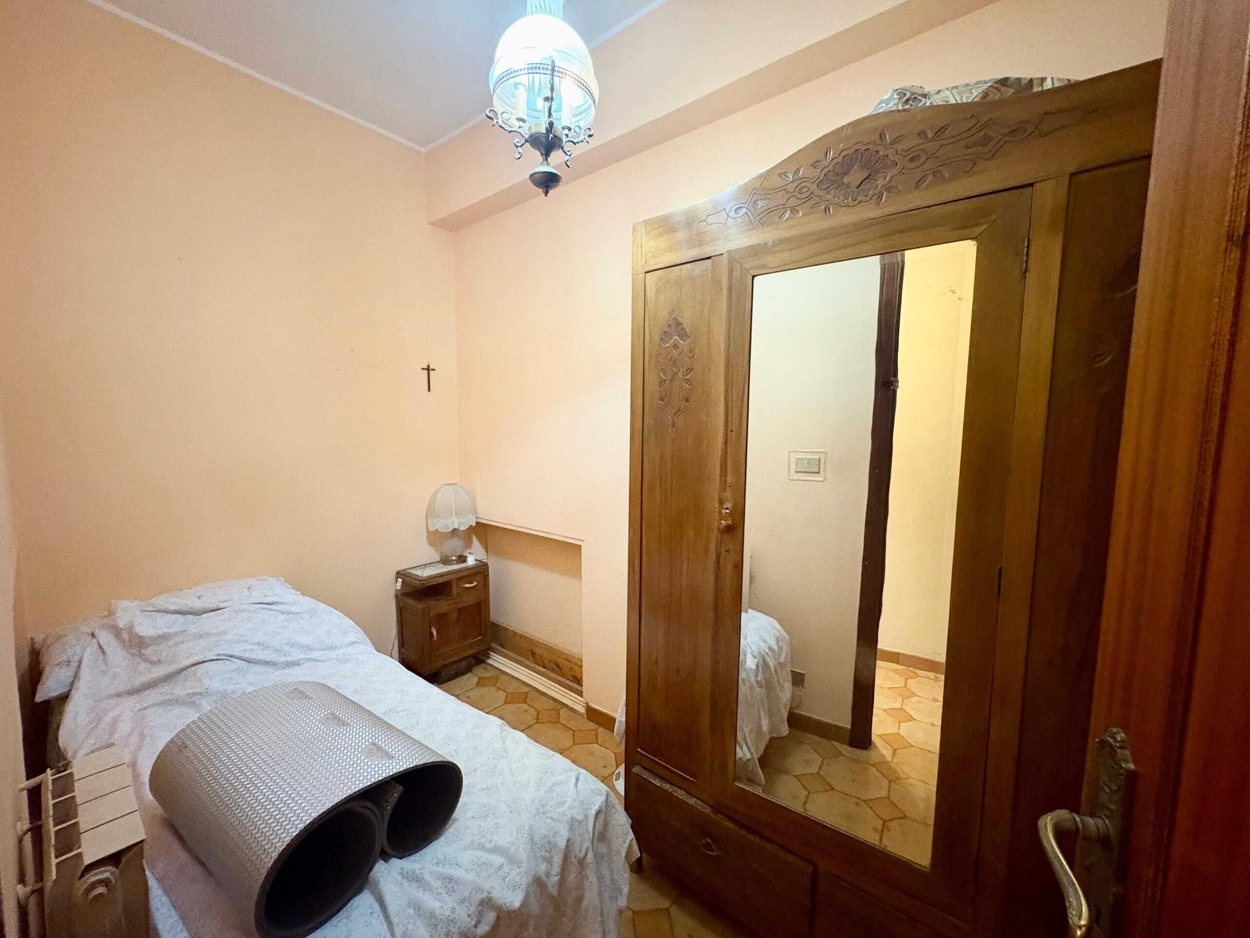 Armadio antico in legno con specchio, camera da letto con pareti beige, letto singolo con biancheria bianca, lampada da tavolo e paraschiena, arredamento rustico, molto accogliente, casa NextCasa.