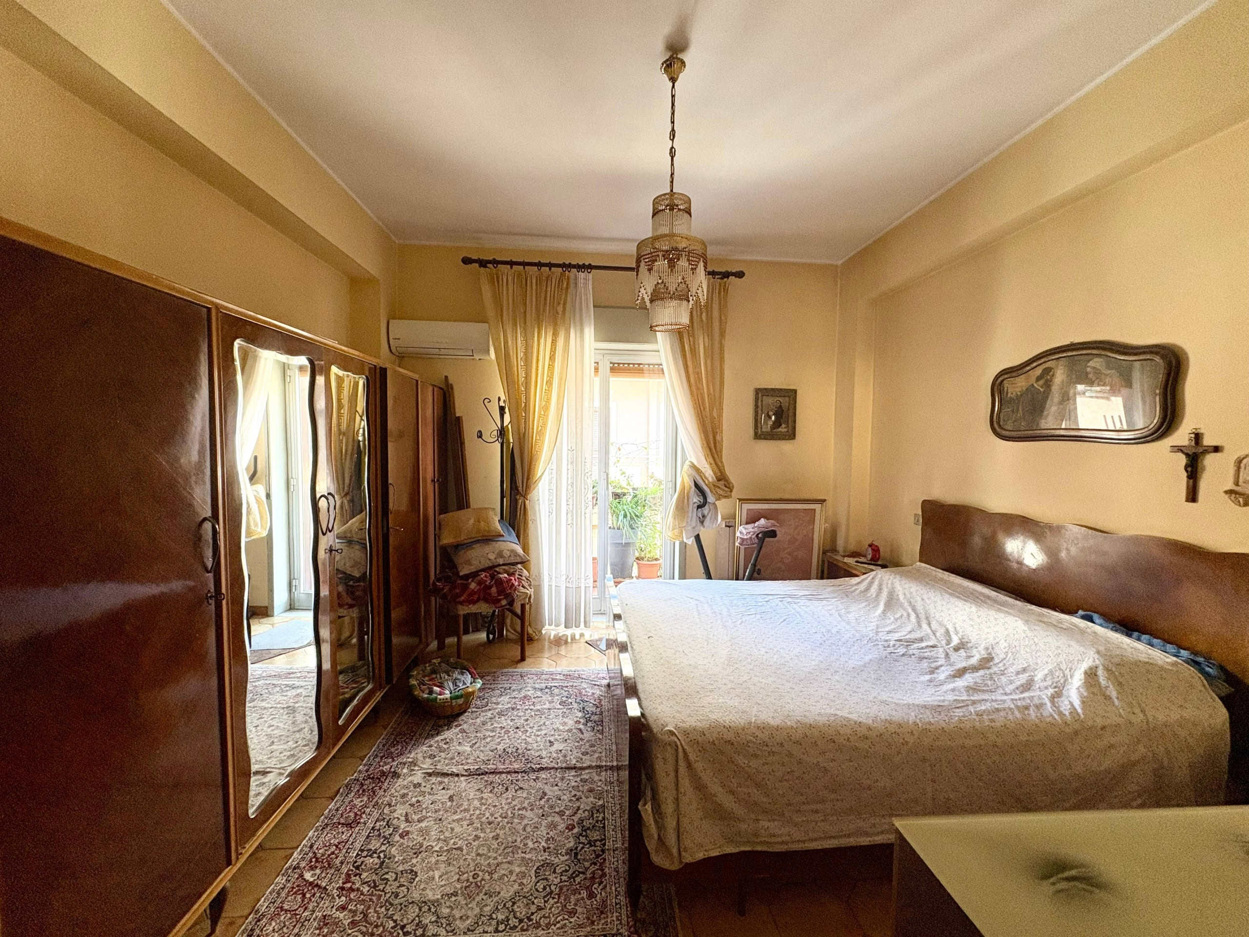 Armadio antico in camera da letto con specchi, letto matrimoniale e accessori vintage, ampie finestre con tende leggere, arredamento classico e atmosfera accogliente in stile vintage.