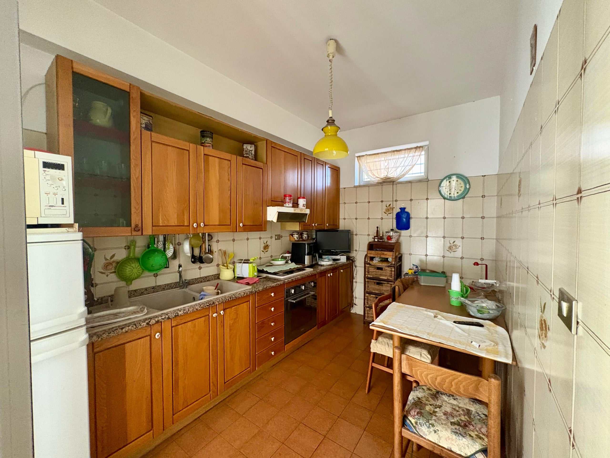 Cucina abitabile in stile tradizionale con mobili in legno, piano in pietra, pareti rivestite con piastrelle carbato, zona pranzo con tavolo e sedie, accessori da cucina e piccoli elettrodomestici.