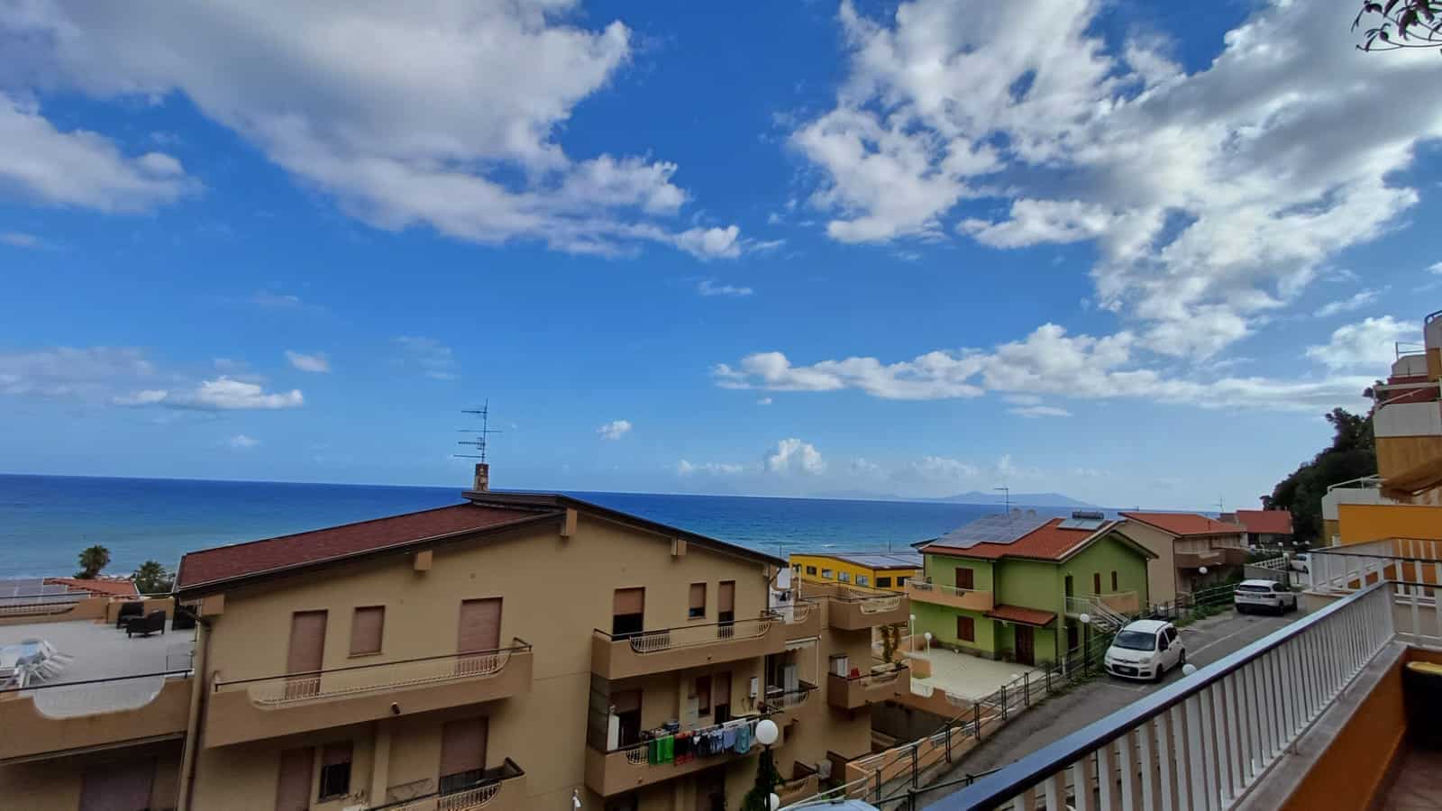Spiaggia e case sulla costa con vista mare, cielo sereno e nuvole bianche, residenze colorate in stile mediterraneo, panorama urbanistico vicino al mare, atmosfera estiva e tranquilla, ideale per vacanze al mare.