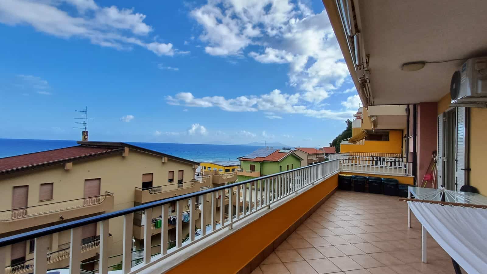 Vista mare dal balcone di un appartamento a NextCasa, con tetti colorati e cielo azzurro. Spazio esterno ampio, perfetto per godersi il panorama e il clima mediterraneo.