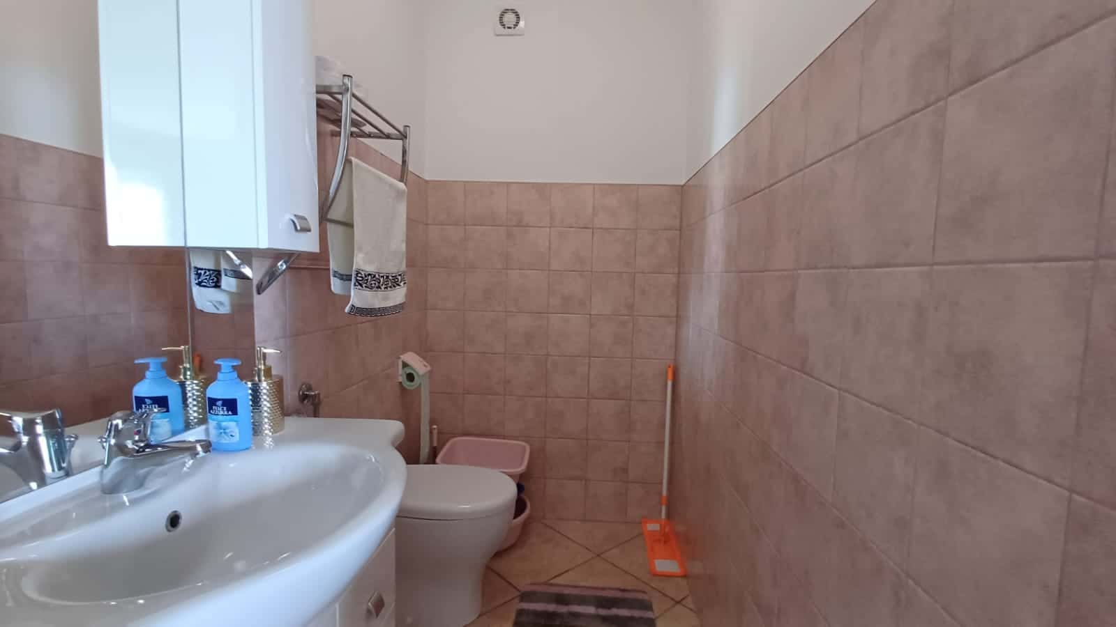 Lavabo e sanitari in un bagno moderno con pareti rivestite in piastrelle beige, accessori eleganti e servizi igienici funzionali. Ideale per arredare con stile e comfort ambienti bagno di case e appartamenti.