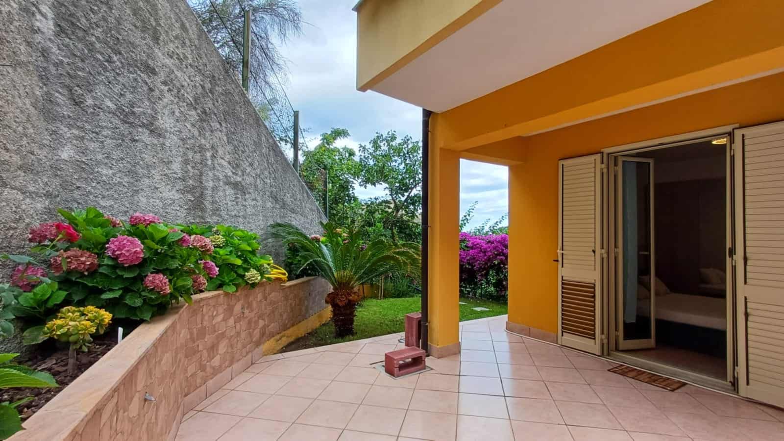 Fioriere con piante fiorite sul balcone di una casa moderna con pareti gialle e viste sul giardino rigoglioso, ideale per annunci immobiliari e appartamenti in vendita.