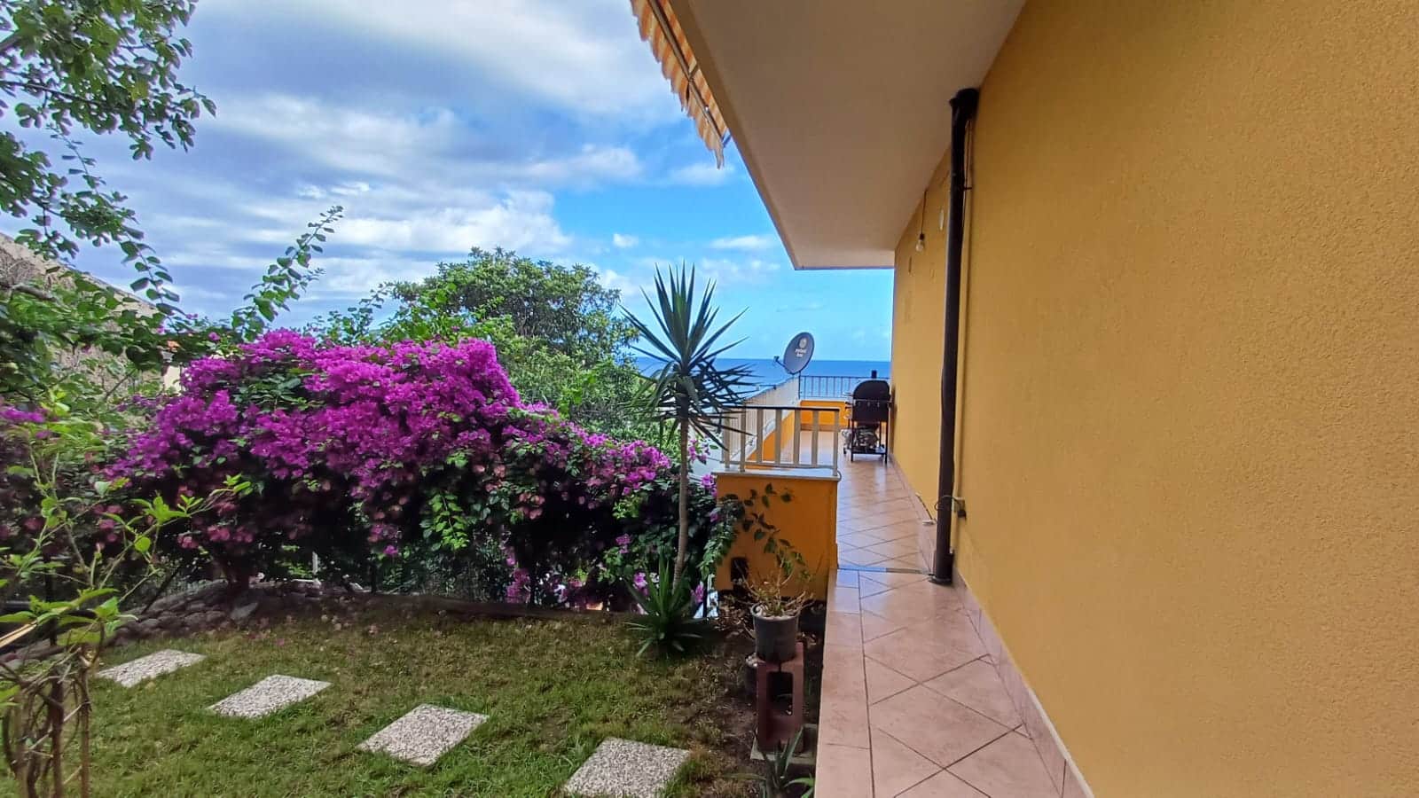 Balcone di casa con vista mare, piante tropicali e fiori colorati, ideale per relax e outdoor, in un ambiente accogliente e luminoso, perfetto per vivere l'estate in comfort.