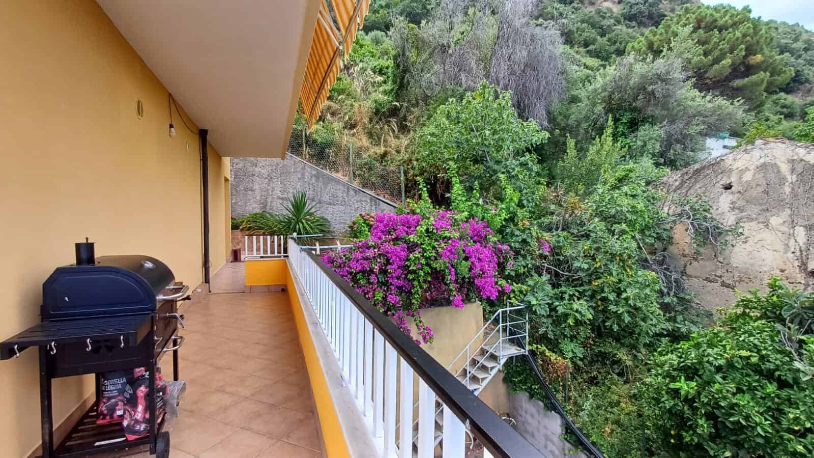 Balcone con barbecue e vista su verdeggiante natura e piante fiorite.
