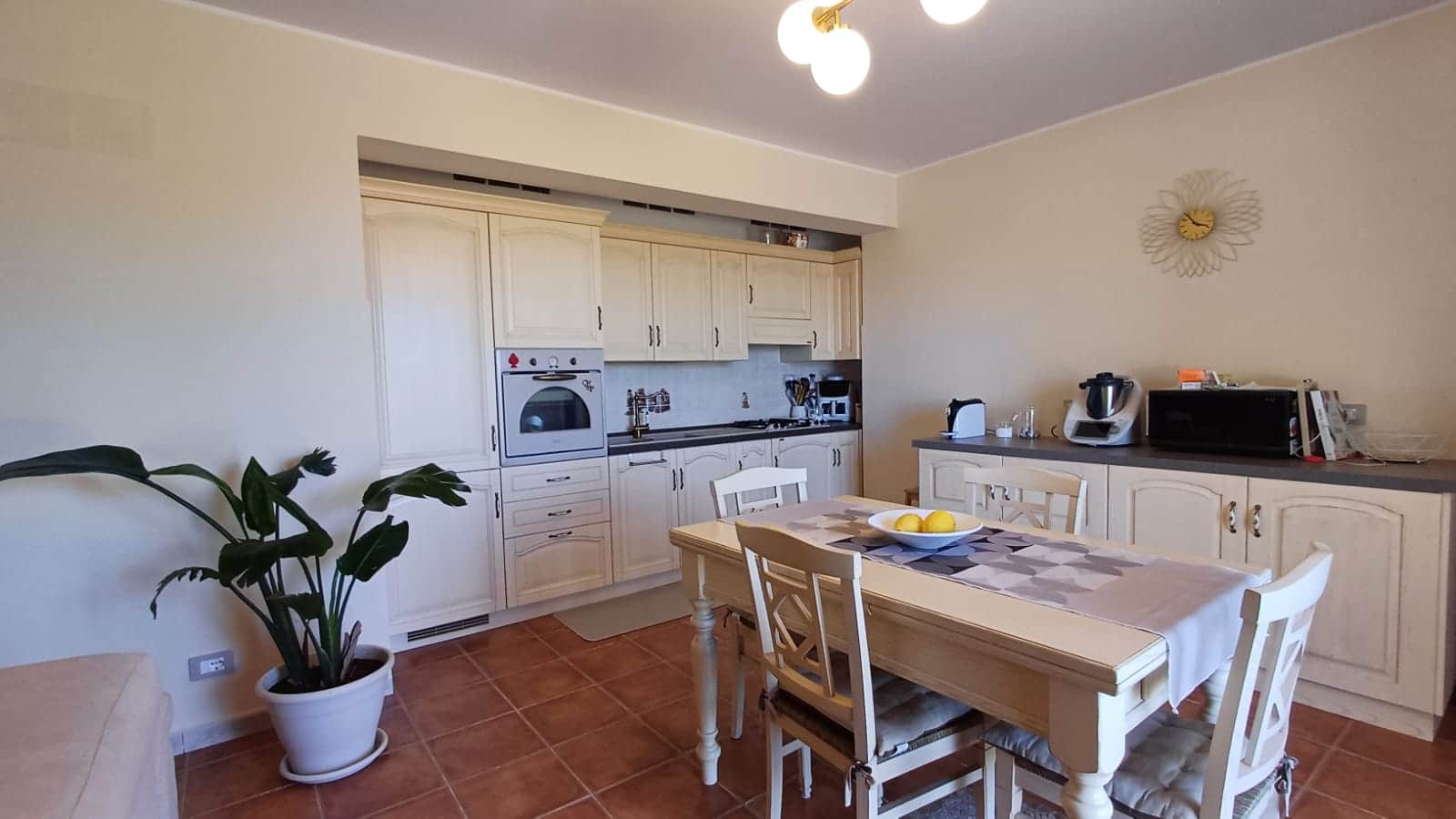 Spazio cucina arredato con mobili in stile classico, tavolo da pranzo con sedie, elettrodomestici moderni, ambiente luminoso e accogliente, ideale per vivere in comfort.