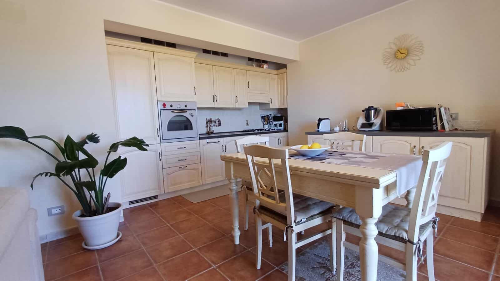 Soggiorno cucina in stile classico con mobili color avorio, tavolo da pranzo, elettrodomestici moderni e pareti beige, ambiente accogliente e funzionale per la casa.