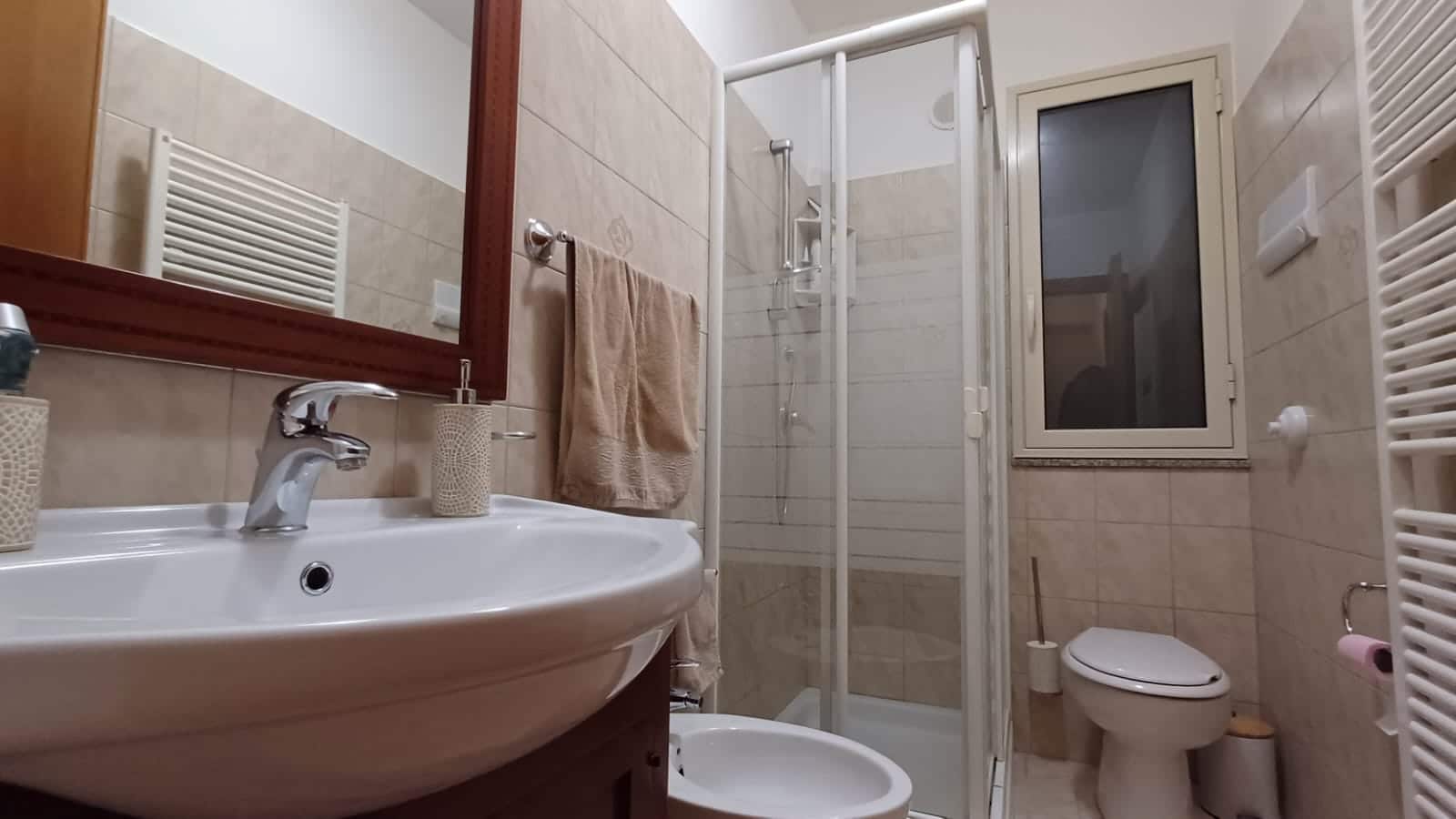 Bagno moderno con doccia, lavabo e servizi igienici in un ambiente accogliente, con finiture beige e arredi funzionali, ideale per residenze e affitti brevi.