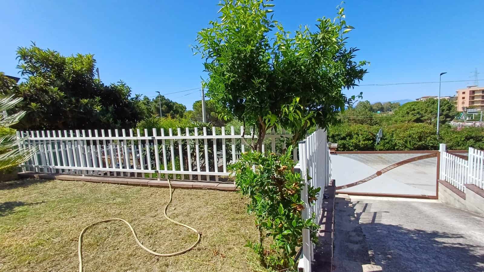 F Khôngسى giardino esterno con siepe, piante verdi e recinzione in ferro bianco, ambiente luminoso e tranquillo, ideale per case o immobili residenziali, vista panoramica su aree verdi e città.