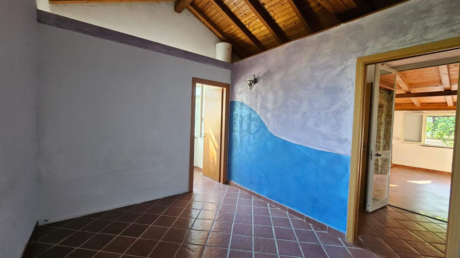 Muri interni di una casa con pareti dipinte con effetto pittura artistica, soffitto in legno con travi a vista e pavimento in terracotta, ambienti luminosi e accoglienti.