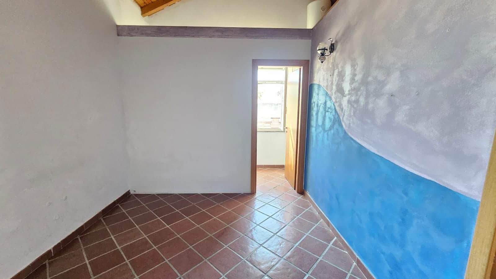 VANO INTERNO DI UNA CASA CON PARETE PAINTED A MURO AZZURRO E BIANCO, INGRESSO A PORTA IN LEGNO CON FINESTRA NATURALE, PAVIMENTO IN Piastrelle di terracotta, atmosfera luminosa e accogliente.