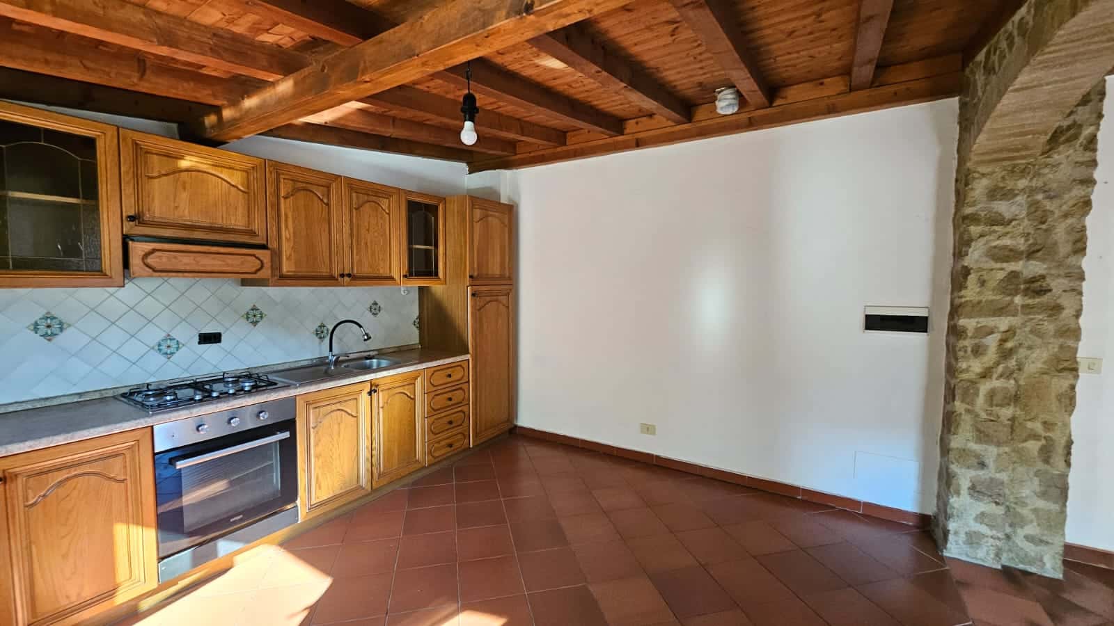 Cucina in stile rustico con armadi in legno, piastrelle decorative e accessori moderni, ambiente accogliente e luminoso, perfetto per la vita quotidiana.