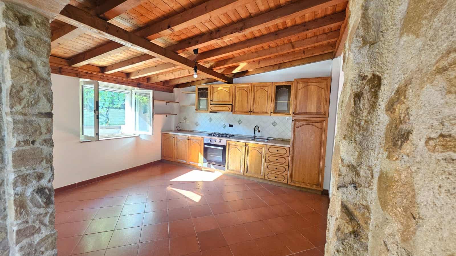 50. cucina rustica in stile tradizionale con mobili in legno, parete in pietra, soffitto con travi in legno e grande finestra per luce naturale NextCasa.