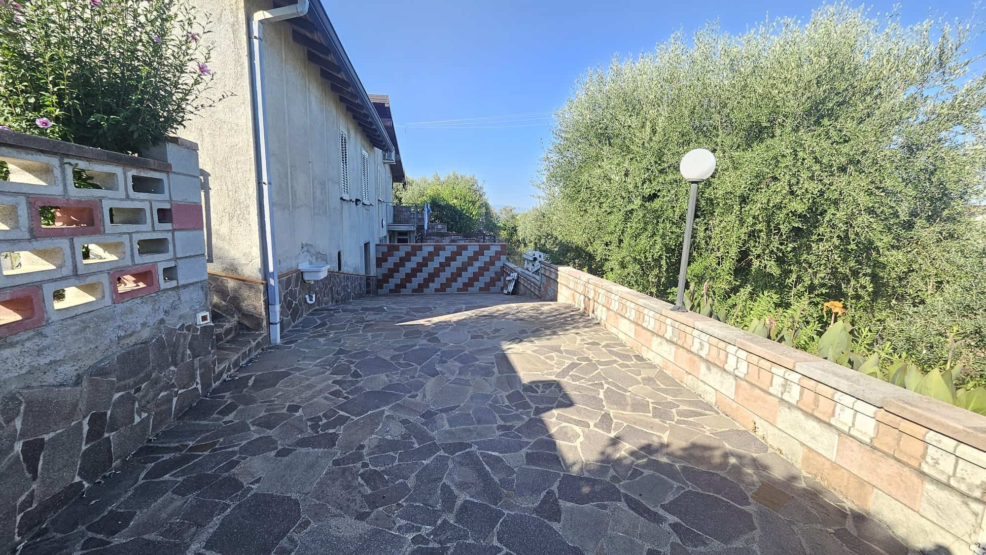 Ampio terrazzo con pavimentazione in pietra e vista su alberi, ideale per relax e socializzare all'aperto, in zona residenziale tranquilla, con illuminazione pubblica e privacy garantita.