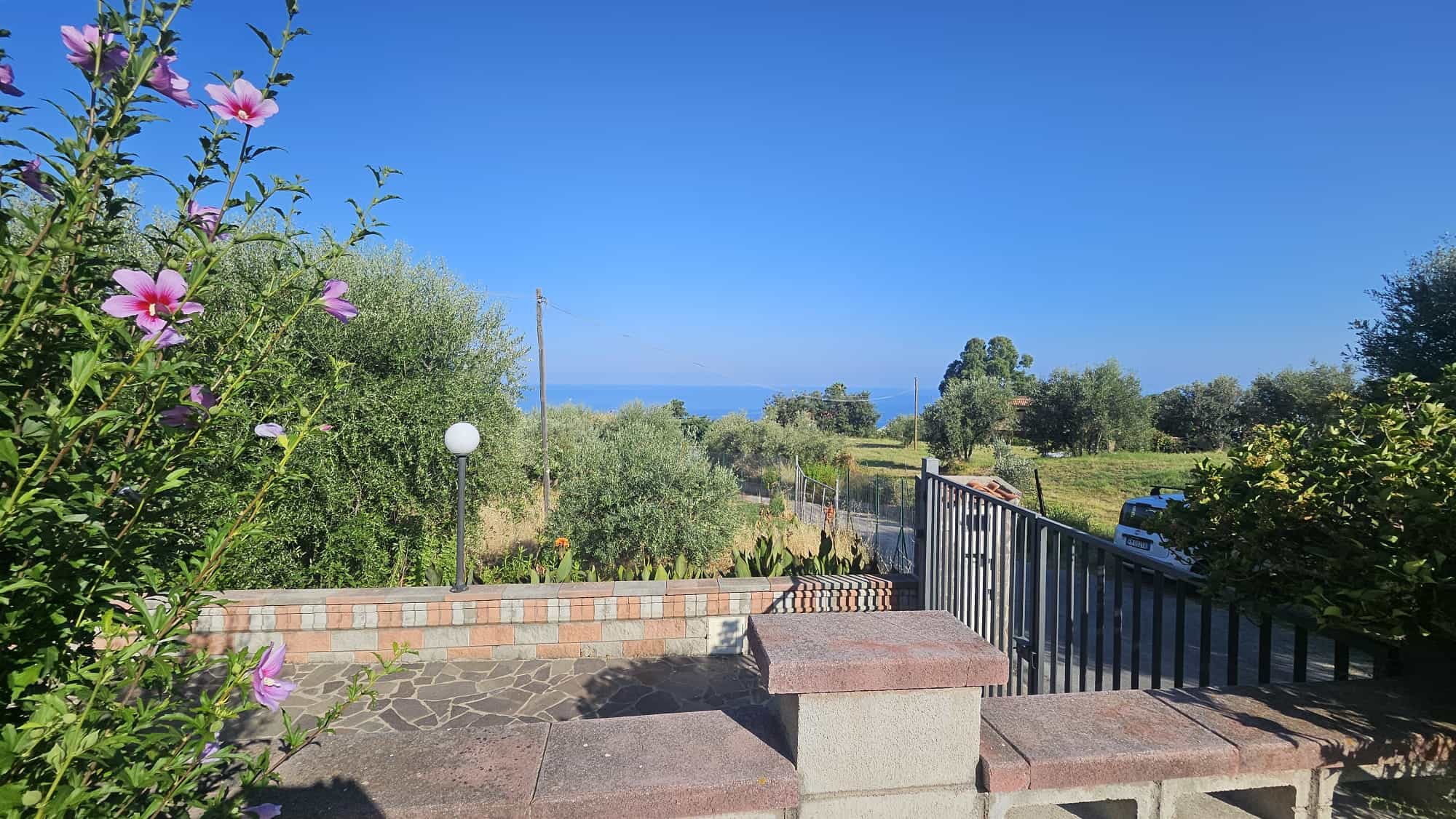 Veranda con vista panoramica sul mare, giardino rigoglioso e paesaggio rurale, ideale per case vacanze e immobiliare a NextCasa.