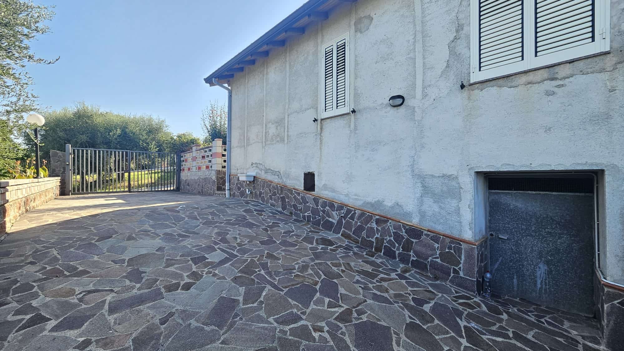 Vasto cortile esterno in pietra per garage e ingresso casa, con recinzione e giardino, ambiente residenziale, spazi esterni curati e pratici, ideale per abitazioni e immobili di pregio.