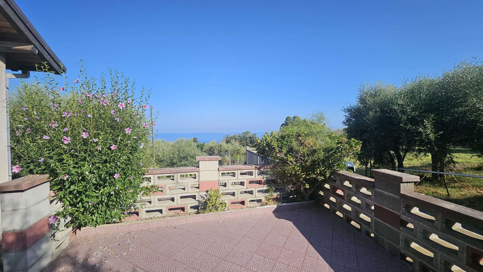 Finestra con vista sul giardino e sul mare, spazio esterno con piante e fiori, atmosfera tranquilla e rilassante nel contesto di una casa in campagna vicino alla costa, ideale per vivere contatto con la natura.