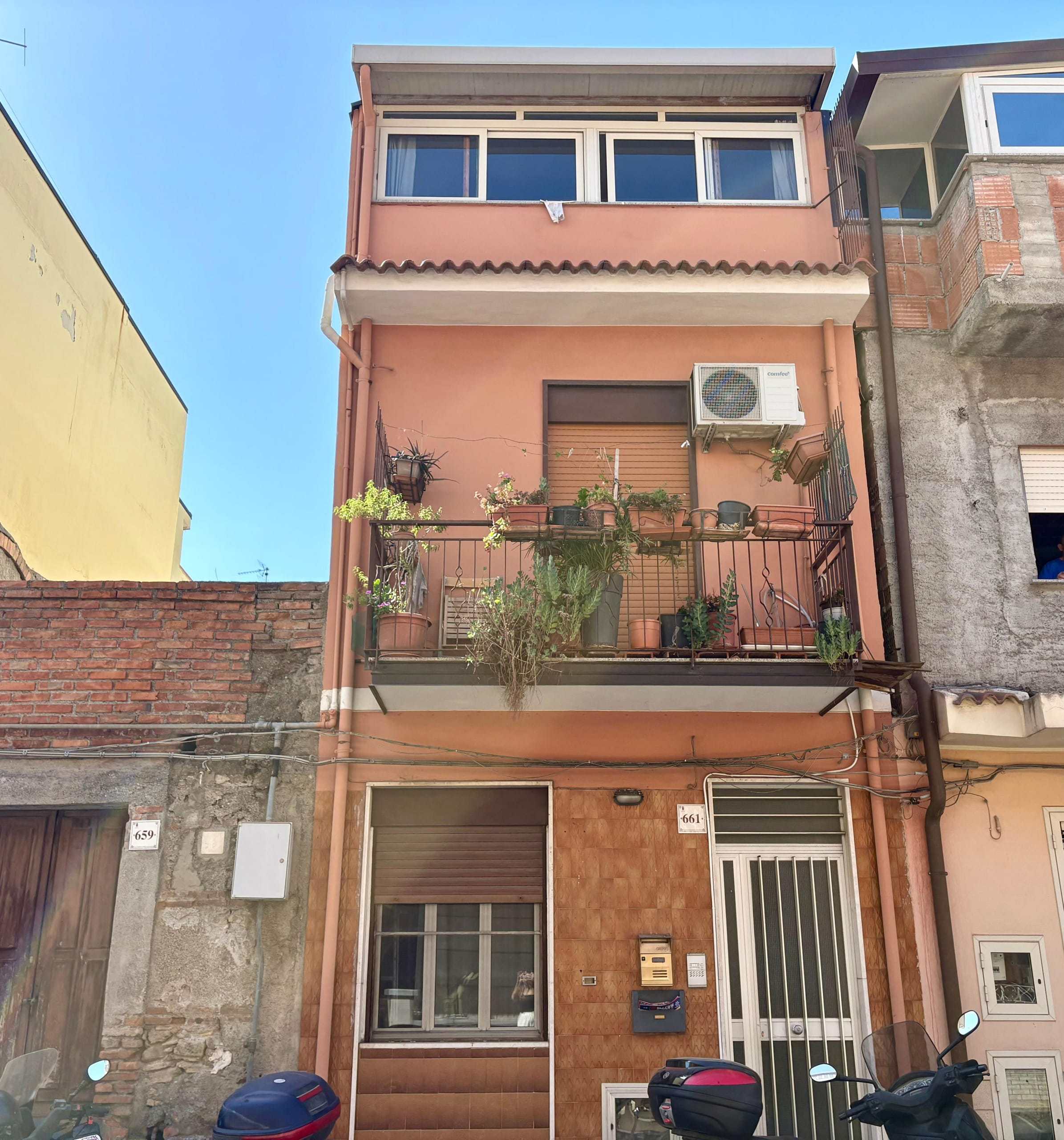 Balcone di un appartamento in edificio urbano con piante e decorazioni, vista su strada con motoscafi parcheggiati, ambiente residenziale, immobile di città, esempio di balcone con piante e stile abitativo.