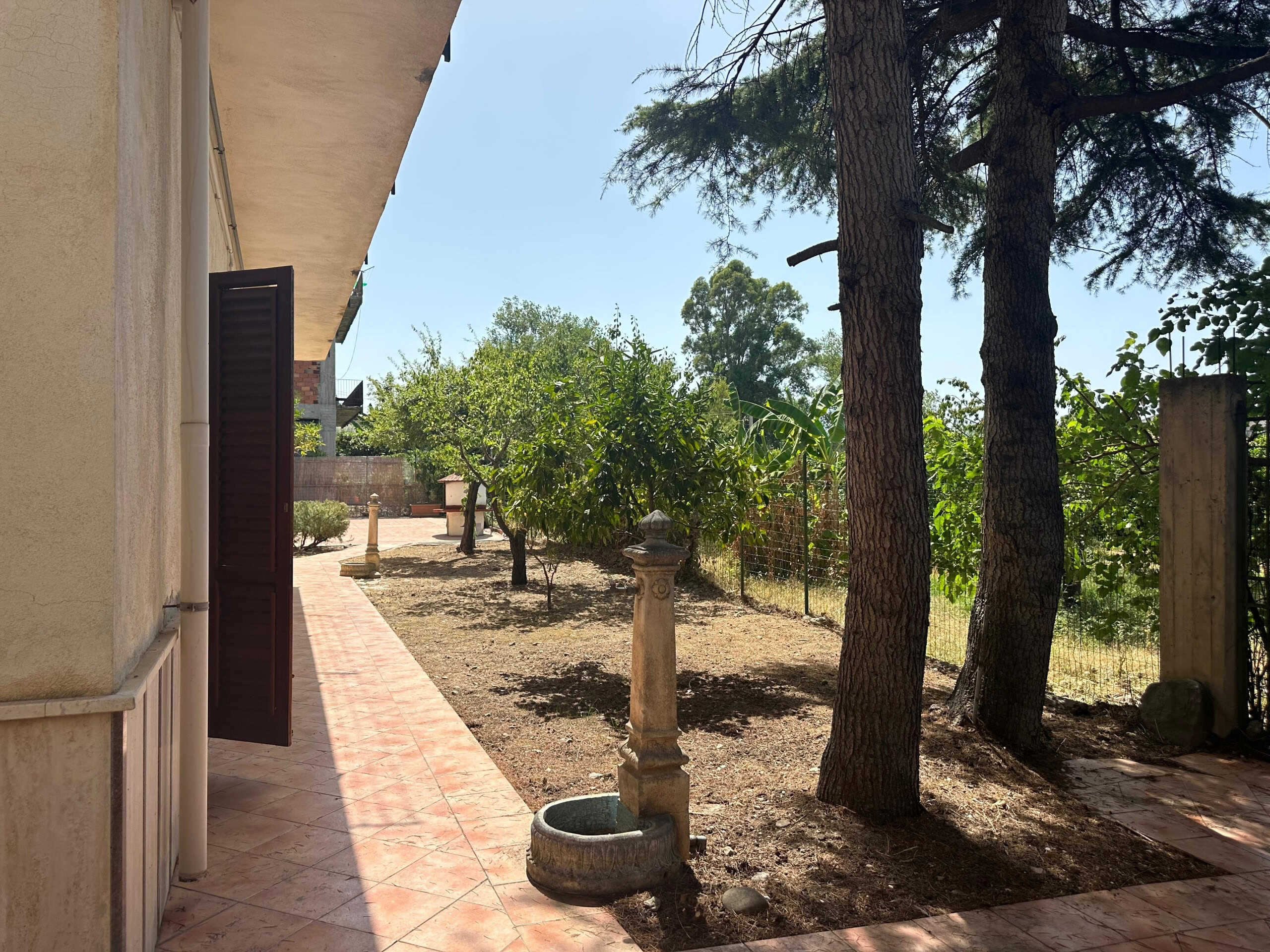 Panorama di giardino privato con alberi e panchine, vista esterna di casa con veranda e spazio verde tranquillo, ideale per vita all'aperto e relax.