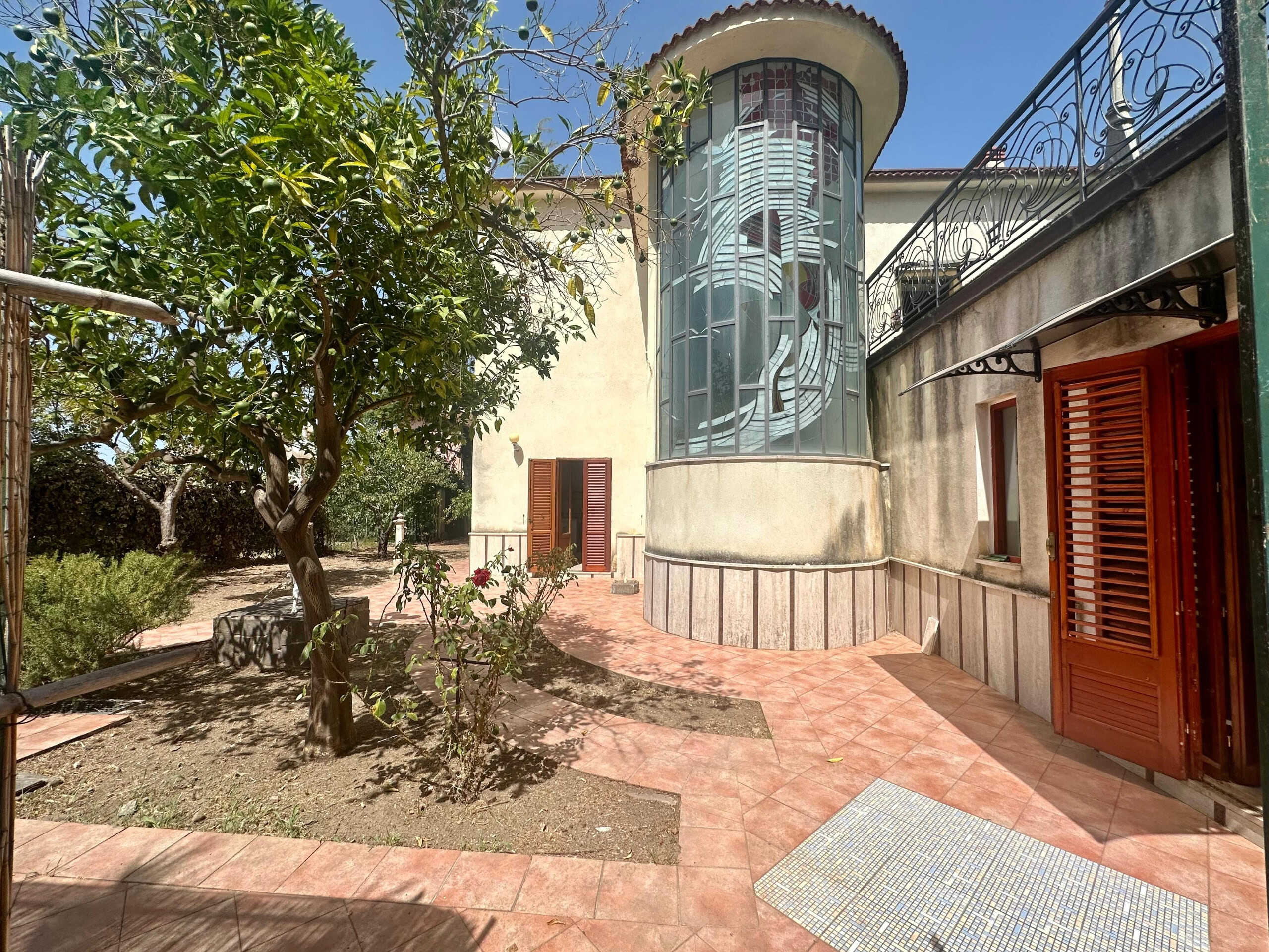 Animale da giardino con alberi, patio in cotto, casa con finestra artistica in vetro e persiane in legno, spazio esterno con area relax, atmosfera tranquilla e residenziale a NextCasa.