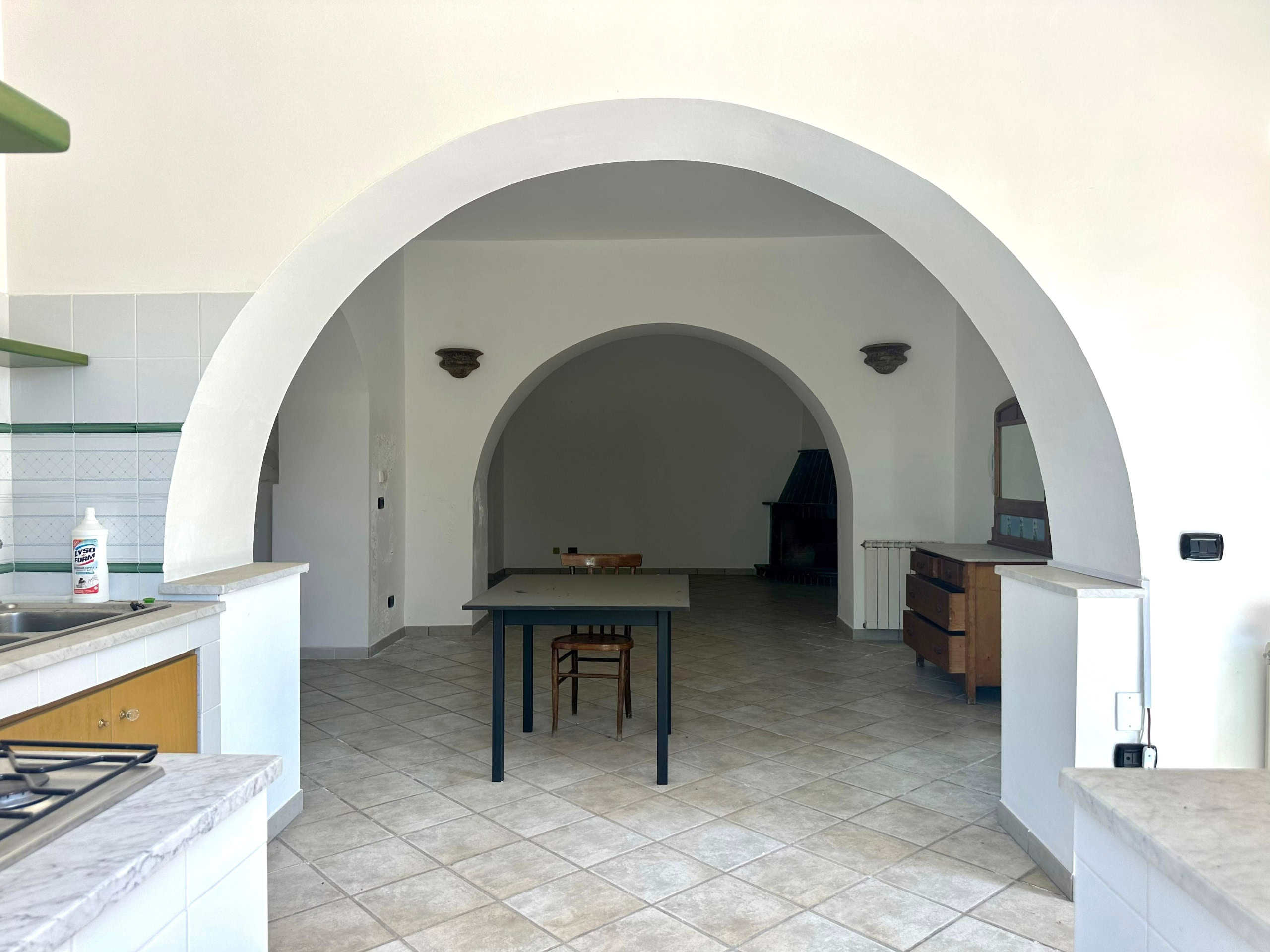 Archi in mattoni e pareti bianche di una cucina abitabile con grandi arcate decorative, pavimento in piastrelle e mobili rustici, ambiente luminoso e spazioso.